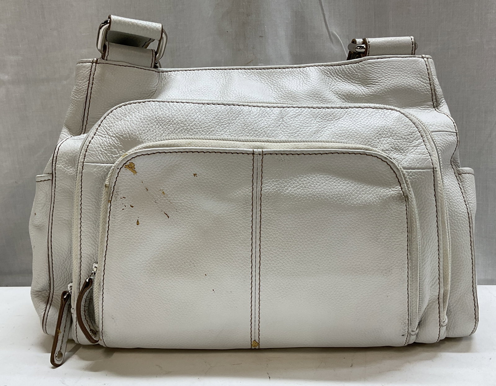 Tignanello White Leather Shoulder Bag: Tignanello white leather shoulder bag. Body is 100% genuine leather. Inside and exterior compartments. Buckle design on straps. Contrast stitching. Side pockets. Zippers and magnetic button closure.