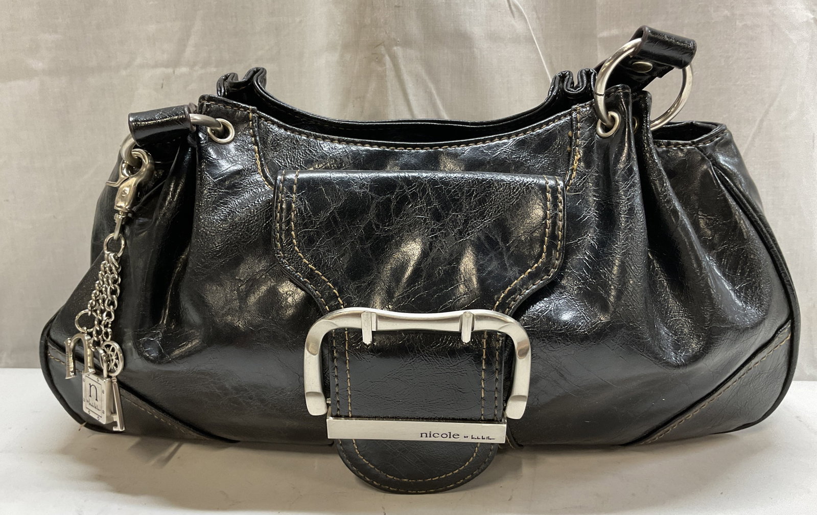 Nicole By Nicole Miller Black Shoulder Bag: Nicole By Nicole Miller black shoulder bag. Accented with silver toned lock and key and N logo key chains. Front buckle accent. Inscriptions on surface. Contrast stitching. Buckle design on straps. Zi