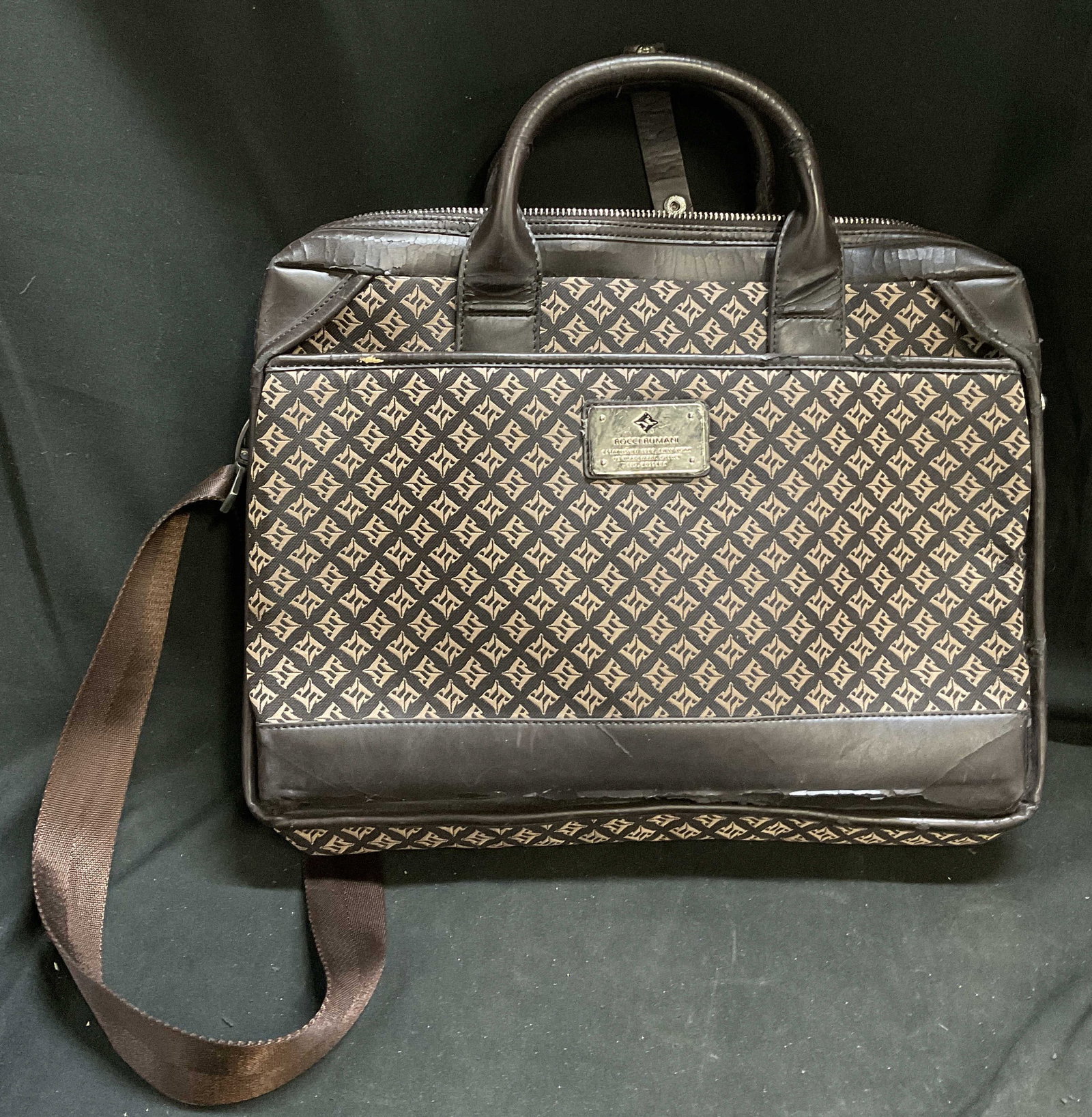 VTG Rocci Rumani Monogram Travel Bag: Vintage Circa 1990s-2000s Rocci Rumani Travel Bag. RR Monogram Pattern on Dark Brown Canvas. Leather-Style Handles and Trim. Silver-Toned Plaque Reads Rocci Rumani Established 1989 New York. Flaking a