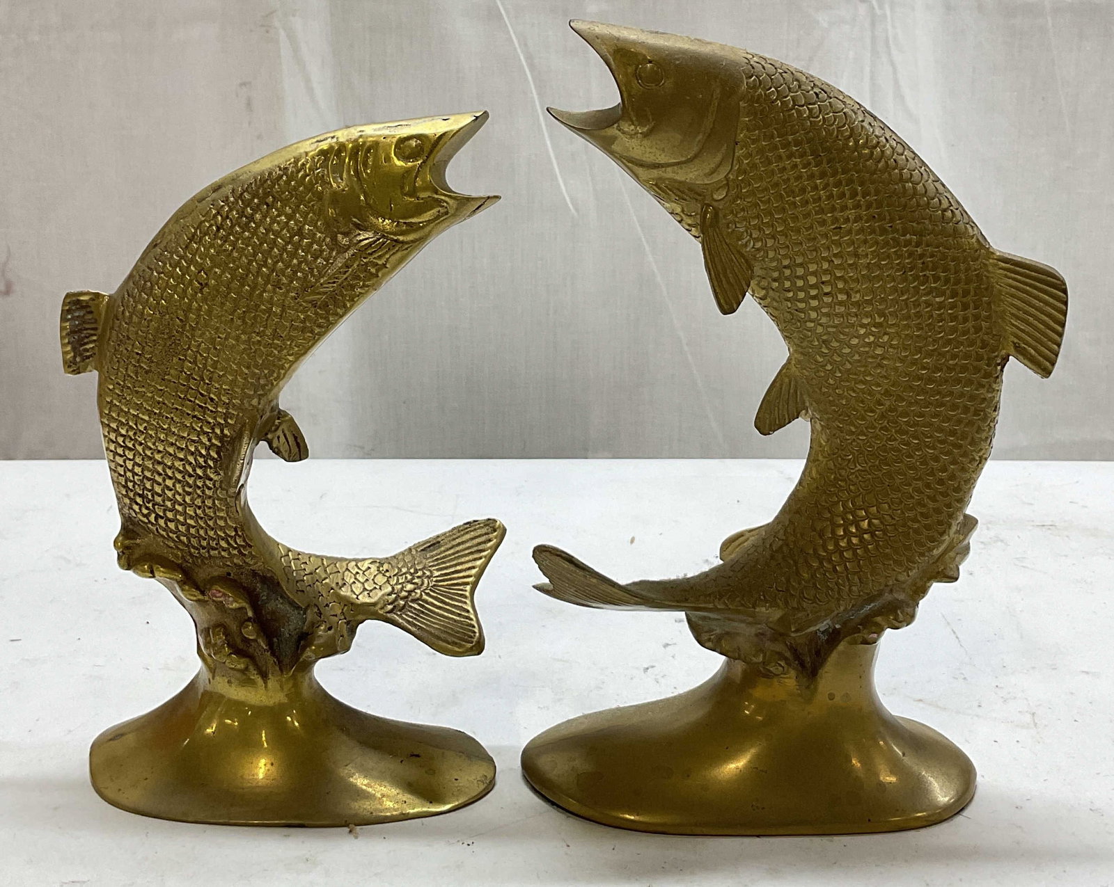 Vintage Brass Leaping Fish Bookends: Vintage brass leaping fish bookends. Oval shaped base. Both fish have their mouth wide open. Detailed textured scale pattern. Curved position. Largest measures approx 3 x 5.5 x 8.5 inches. Surface wea