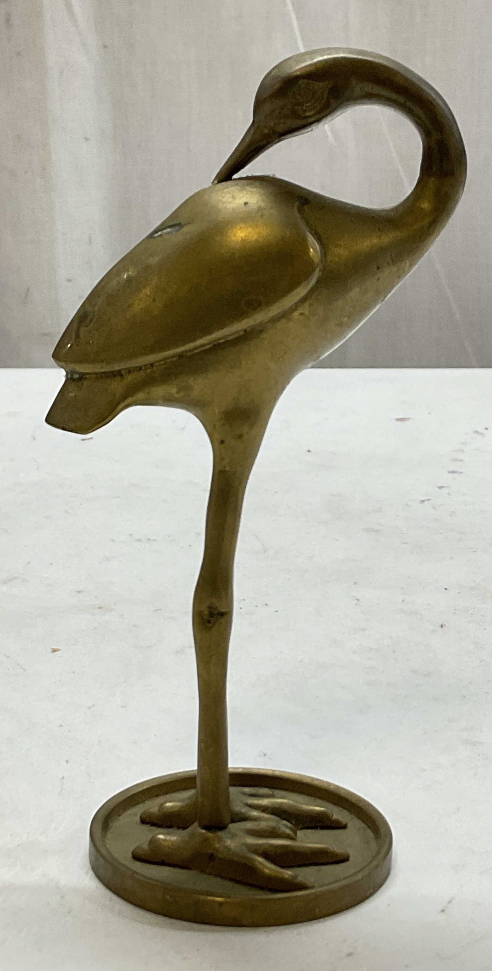Vintage Brass Crane Figure: Vintage brass crane figure. Crane figure with its neck turned backwards, touch its body with its beak. Stands on a circular base. Measures ht approx 5.5 inches diam approx 2 inches. Surface wear