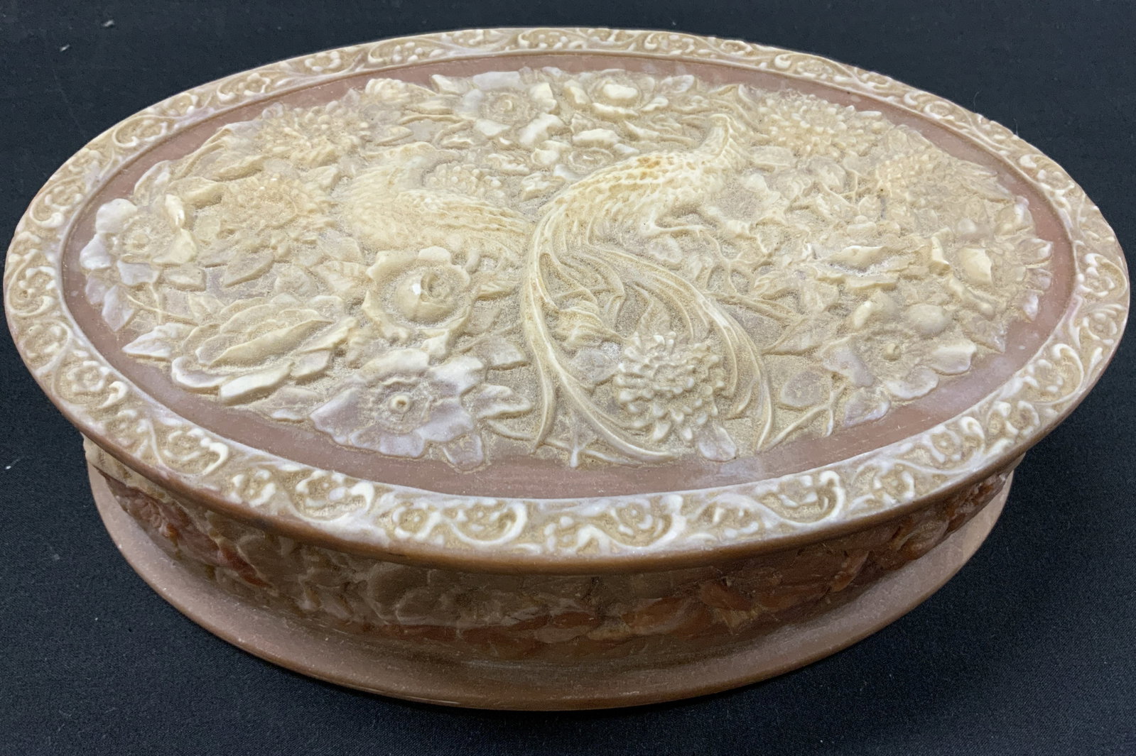 Vtg Incolay Stone Peacock Jewelry Box: Vintage oval Genuine Incolay jewelry box hand crafted USA. Pinkish tan marveled finish with white relief carvings depicting peacock and floral patterns on lid. Side walls detailed eight matching carve