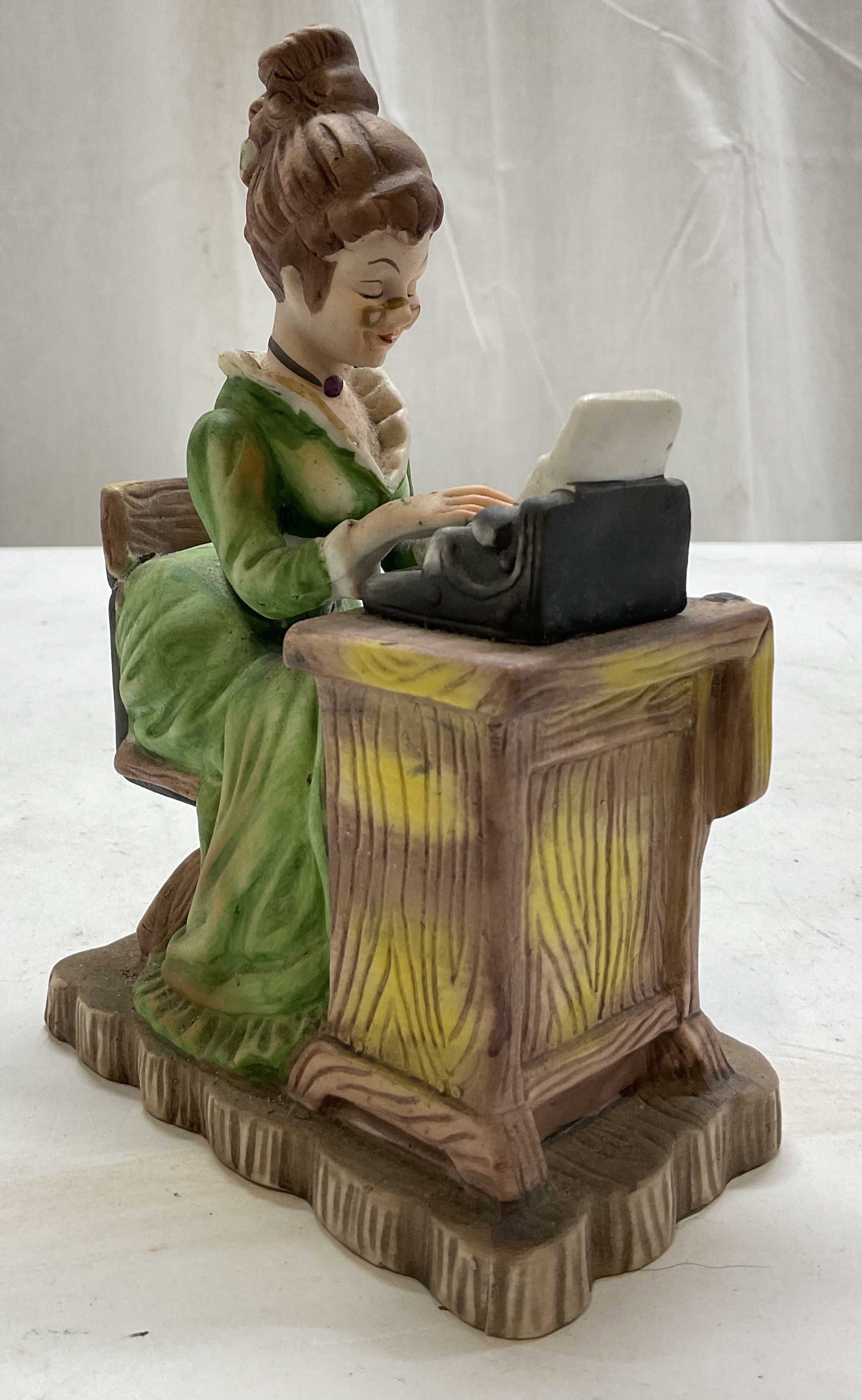 Lefton The Typist Porcelain Figure: Lefton The Typist porcelain figure. Rectangular scalloped base. Depicting a Victorian figure in a green dress typing on a manual typewriter. Hand painted in varying colors. Detailed features. Measures