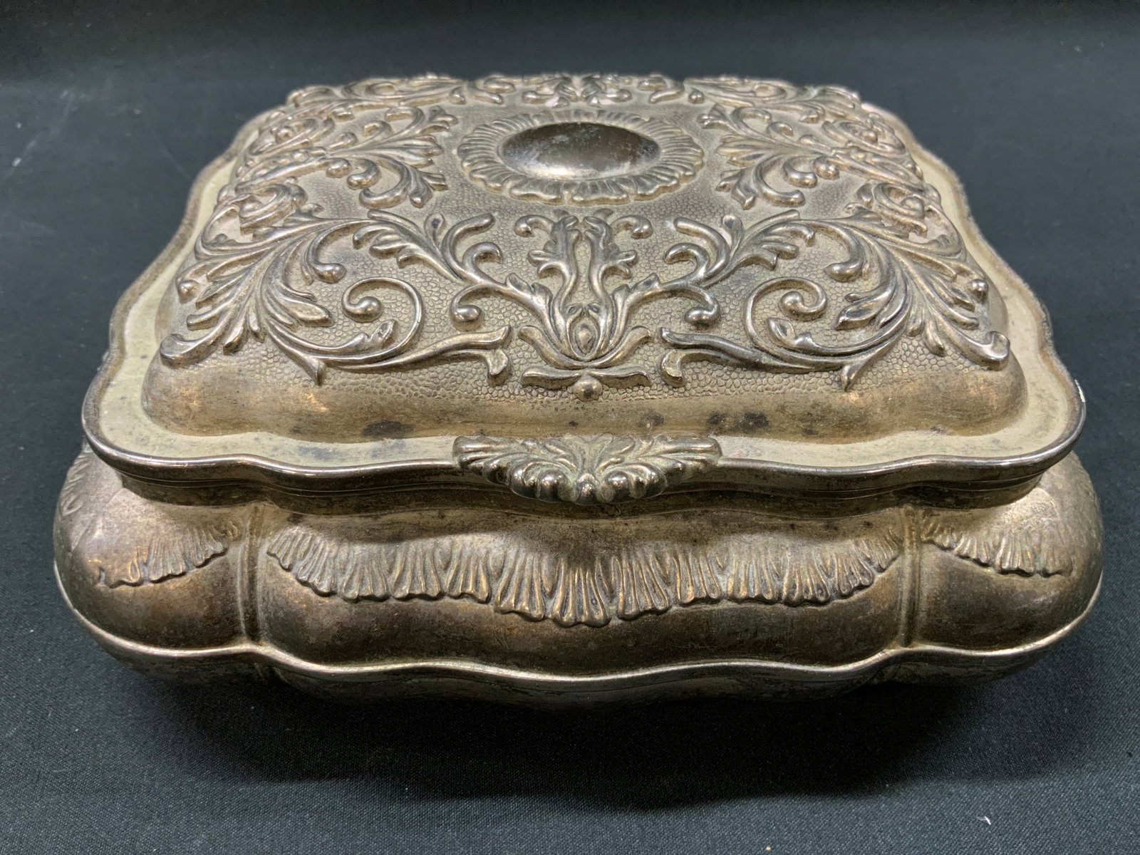 Vtg Repousse Metal Hinged Jewelry Box: Vintage Repousse Metal Hinged Jewelry Box. Square box, embossed scroll and foliate repousse design across lid and scalloped sides. Underside, textured pattern with floral cartouche stamp mark. Red vel