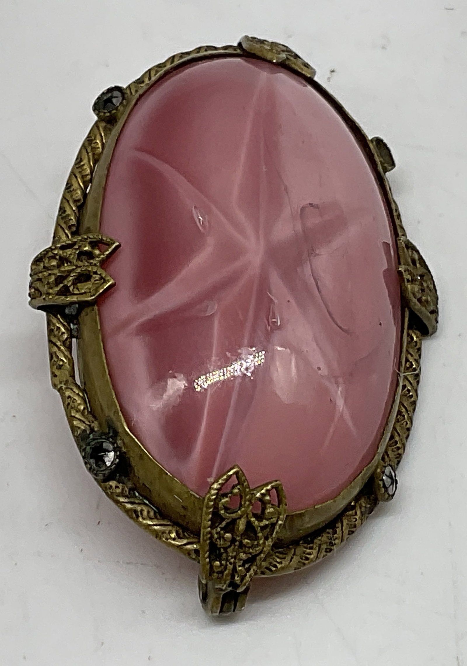 ANTQ Czech Pink Molded Glass Brooch: Antique, Possibly Vintage Czech Brooch. Pink molded glass with starburst pattern center. Brass frame with rhinestone and filigree leaf accents. Missing stone. Oxidization present. clasp closing mechan