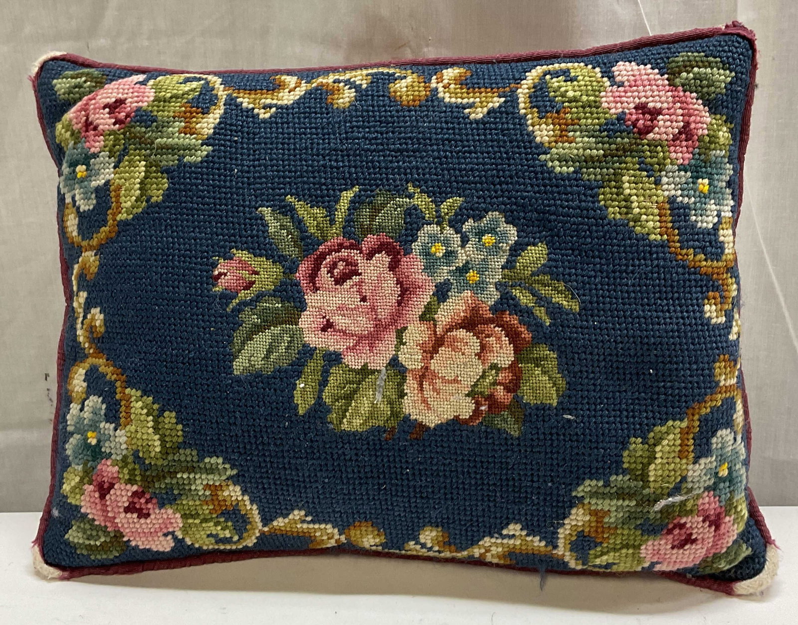 Vintage Navy Blue Floral Needlepoint Throw Pillow: Vintage navy blue floral needlepoint throw pillow. Rectangular shape. Red back. Navy blue background with varying colored floral and scroll motifs. Measures approx 10 x 13 inches. Wear to corners. Thr