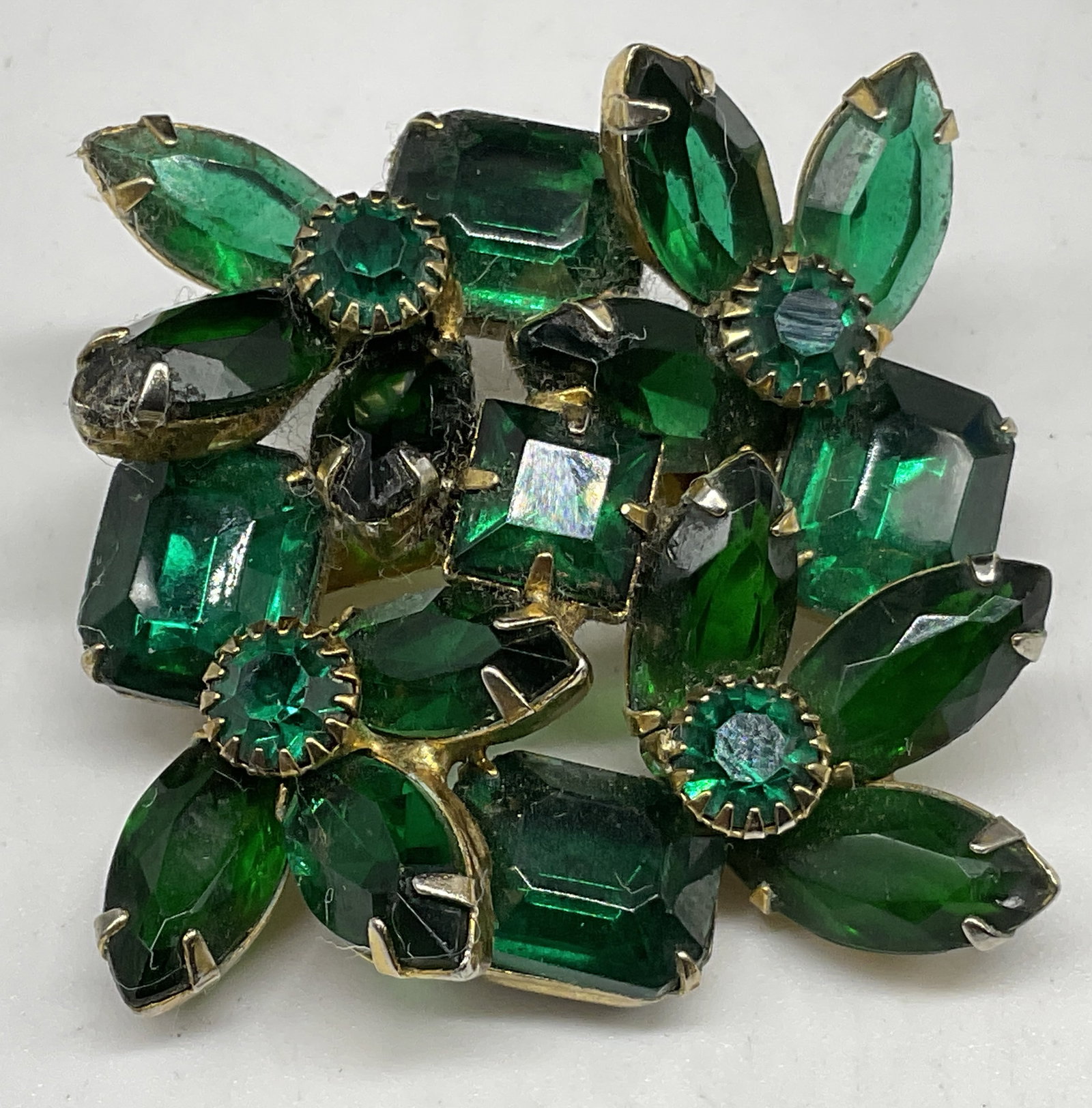 VTG Multi-Tiered Green Rhinestone Cluster Brooch: Vintage Circa 1950s-1960s Multi-Tiered Green Rhinestone Cluster Brooch. Teardrop, rectangular, and circular shaped stones. Gold-Toned frame. Plating loss present. Measures approx 1.5in H x 1.5in L.