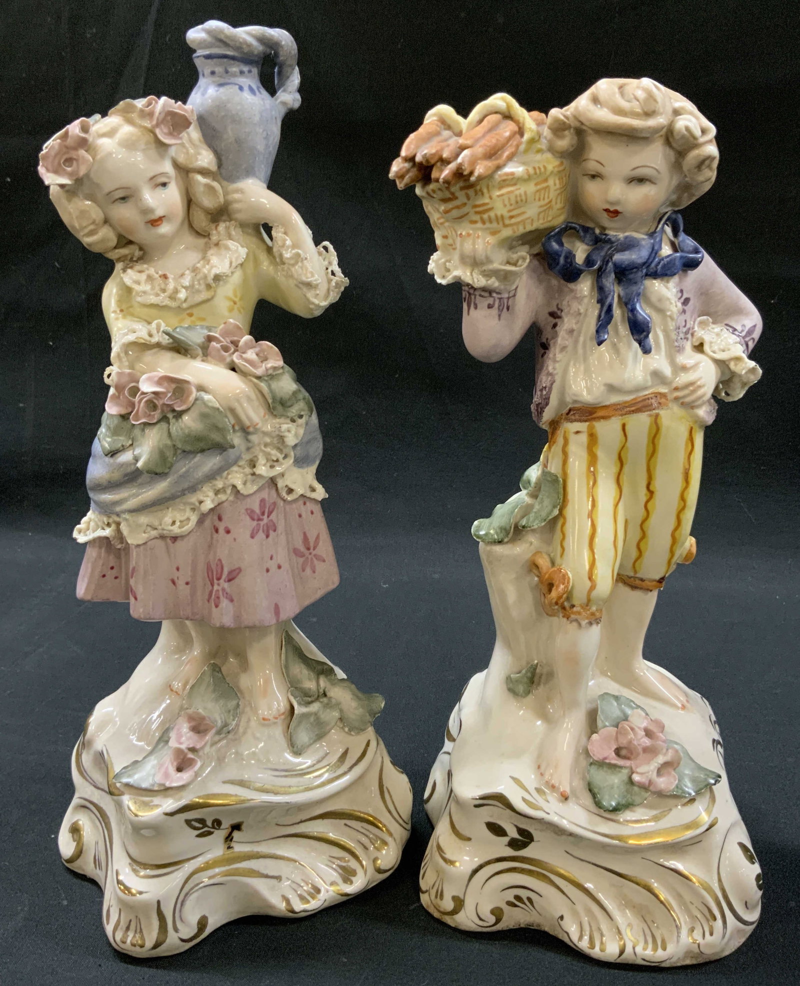 Vtg Lt2 Germany Porcelain Fig. Harvest Couple: Vintage lot 2 matching pair hand painted porcelain figurines of young girl and boy harvesting goods. Female figure carries water jug and florals, Male carries carrots or bread in basket on shoulder. D