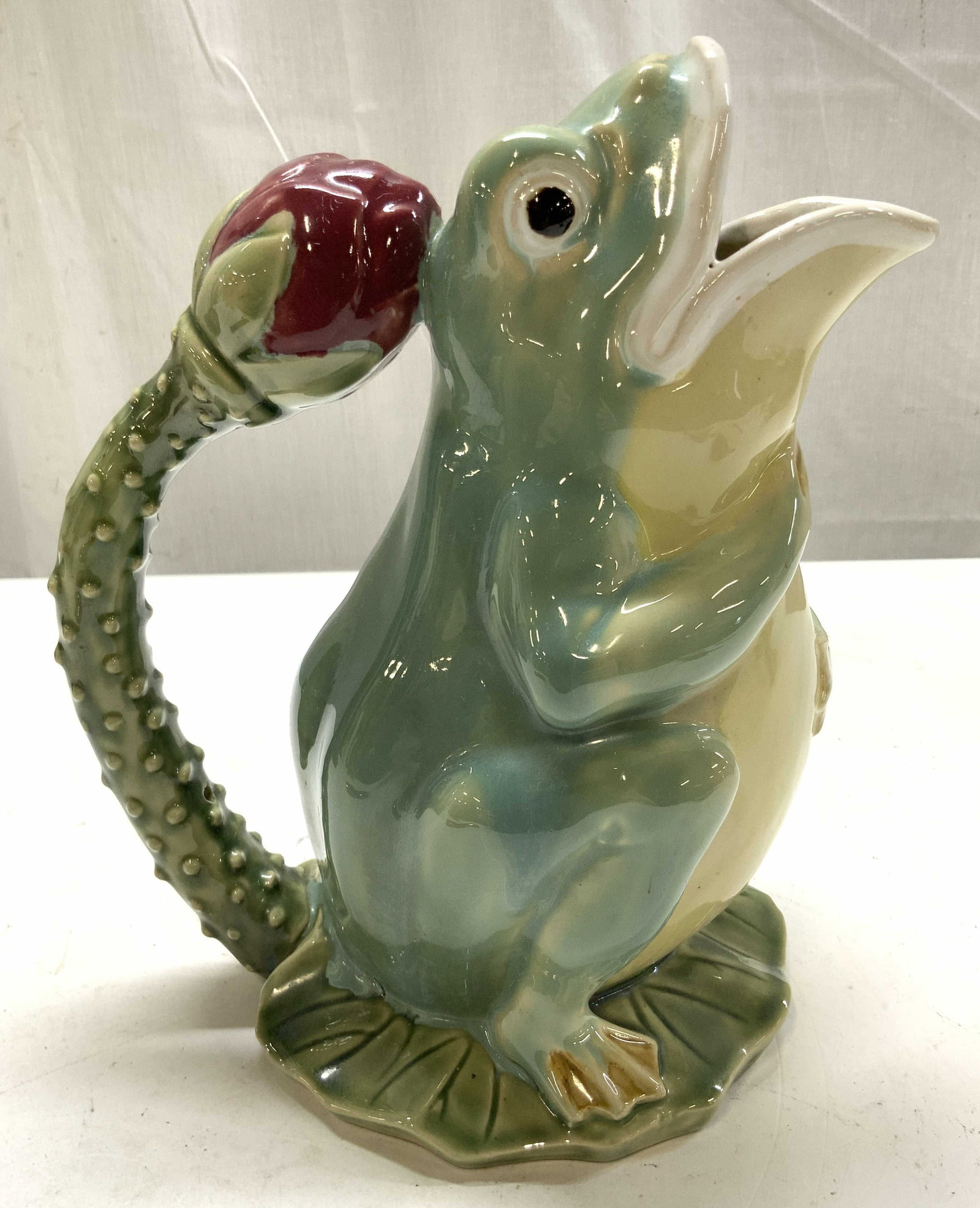 Vntg Majolica Ceramic Frog Pitcher: Vintage Majolica Ceramic Frog Pitcher depicts a glossy green frog perched atop a lily pad base with a spiked rosebud hand lent app 9.5 inches, width app 8 inches, hand painted green and cream glazing