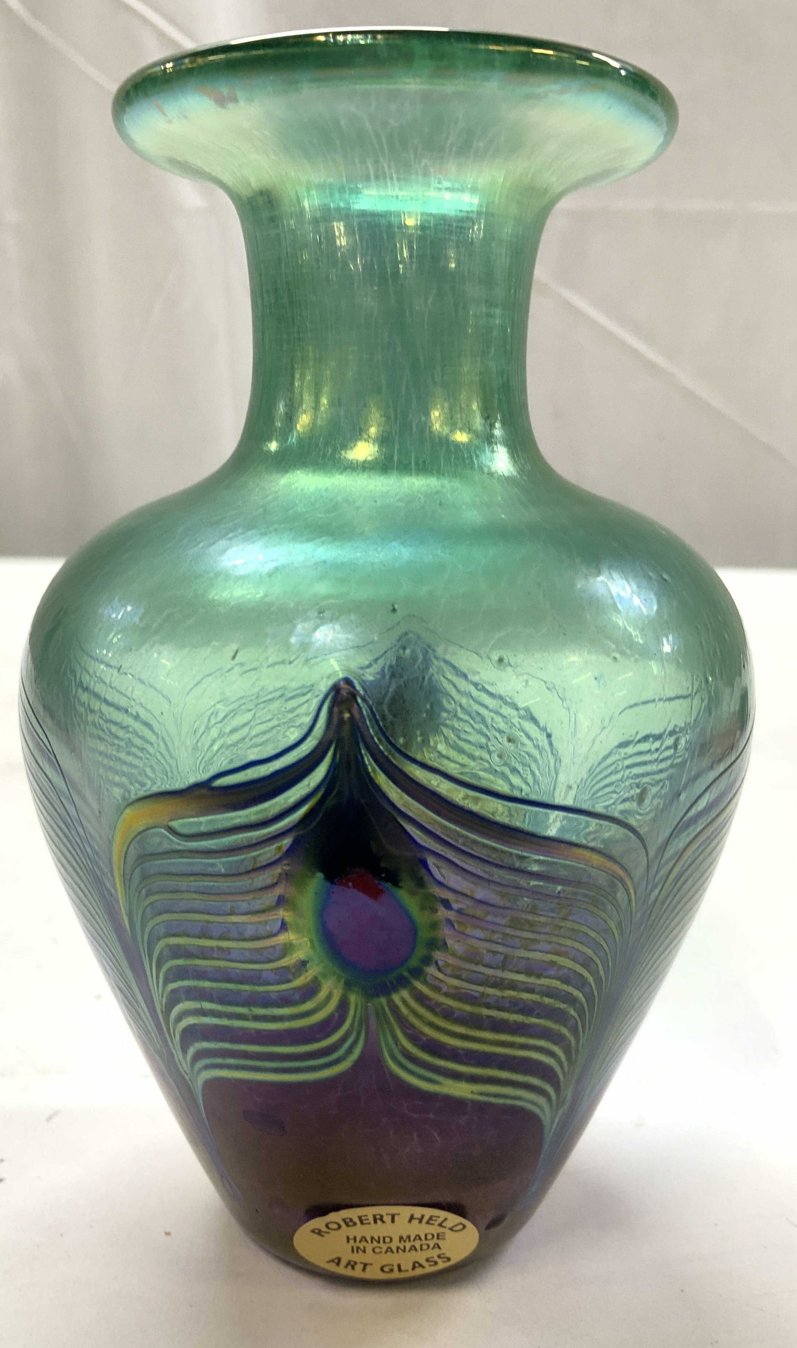 ROBERT HELD Art Glass Peacock Vase, Sgnd: Robert Held hand made Peacock vase, original label on side and signed rim near underside, made in Canada, features an iridescent teal and green finish with an intricate purple and gold pulled feather