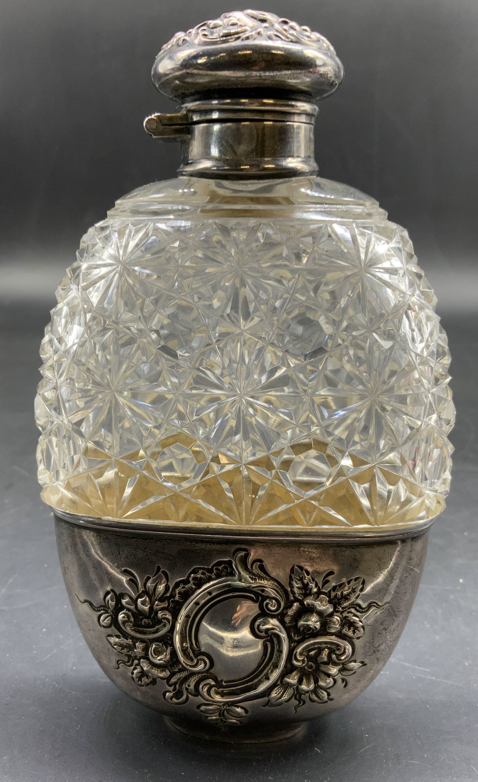 Antique Victorian STERLING and Crystal Flask: Antique Victorian cut crystal and Sterling Silver Flask features An ornate Sterling Silver lower cup, and hinged cap with repousse floral detailing, the upper body is crafted from brilliant heavy crys