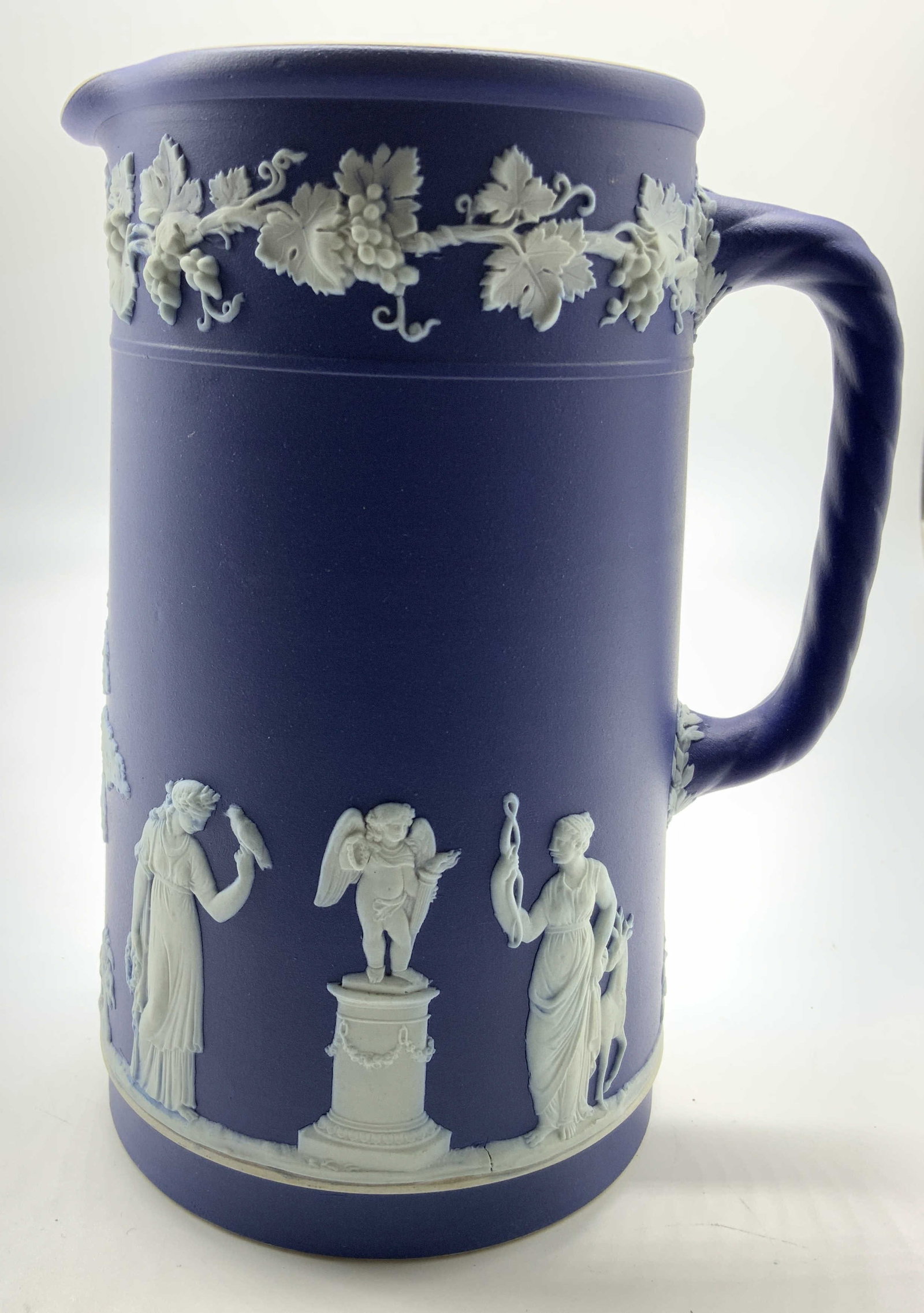 Vntg Dark Blue Wedgwood Jasperware Pitcher: Vintage indigo Wedgwood Jasperware pitcher, signed, featuring white neoclassical relief figures and a delicate grapevine collar, measures ht app 7.5 inches diameter app 6 inches