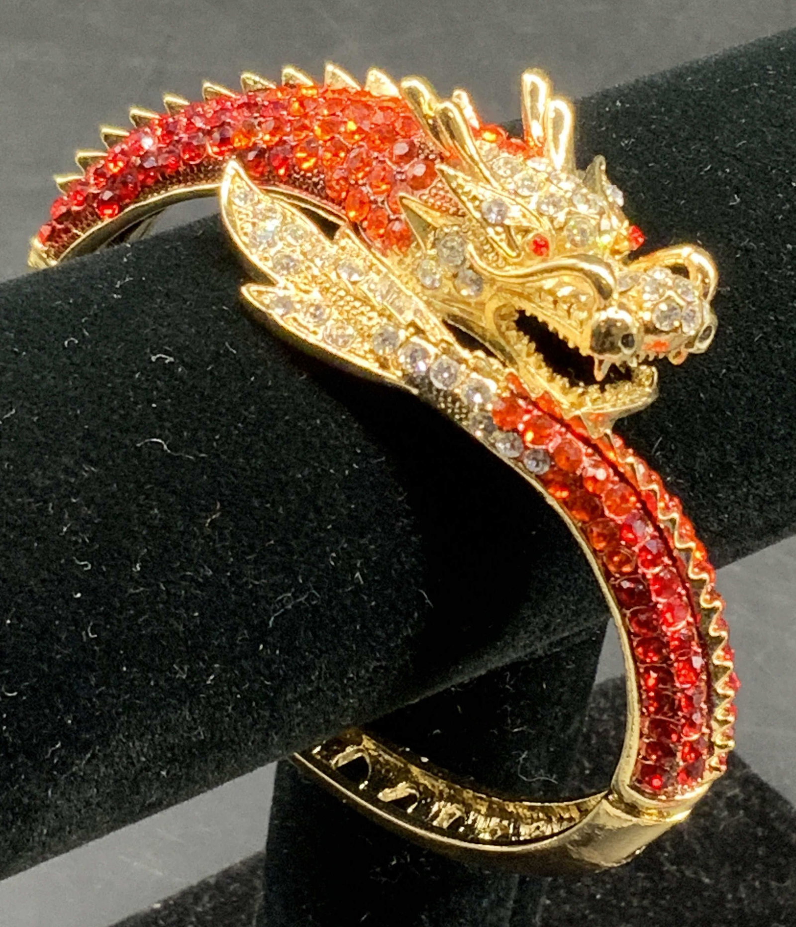 Dragon Gold Tn Rhinestone Bangle Bracelet: Striking gold tone Wrap bangle bracelet, hinge clasp, with sparkling vibrant red rhinestones, features a detailed gold tone dragon head adorned with clear and intense orange red rhinestones, covering