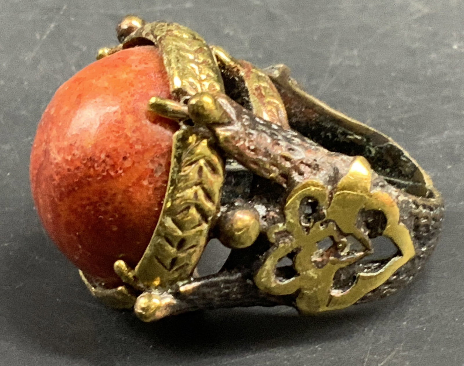 Red Coral Cabochon Statement Ring: Vintage Statement ring featuring an encased large dome cut Ted coral Cabochon set in an ornate gold toned metal mounting, detailed gold and copper toned designed wide band, top measures app 1 inch,