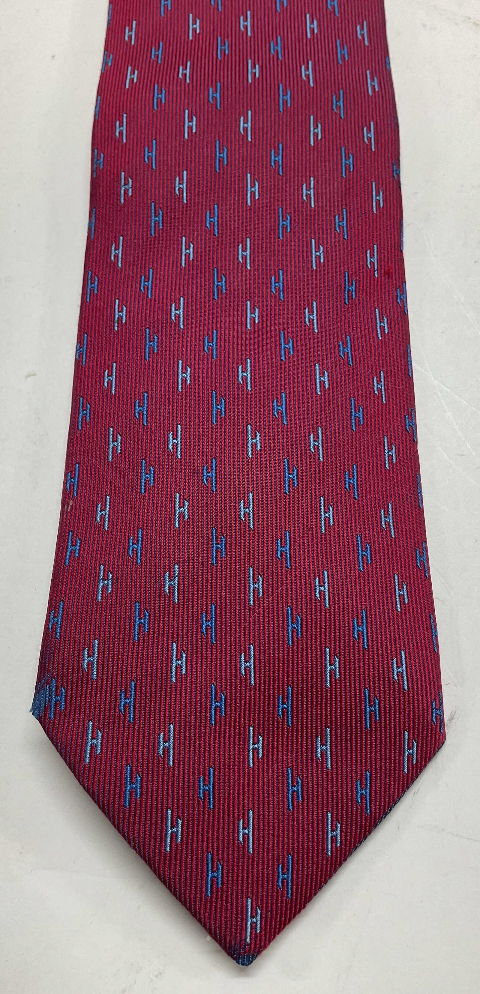 Hermes Red Monogram Silk Neck Tie France: Hermes red monogram silk neck tie. Made in France. 100% silk. Red striped background with repeating blue H monogram. Measures approx 3.5 x 61 inches. Blemishes. Neck tie, silk neck tie, Hermes, wearab