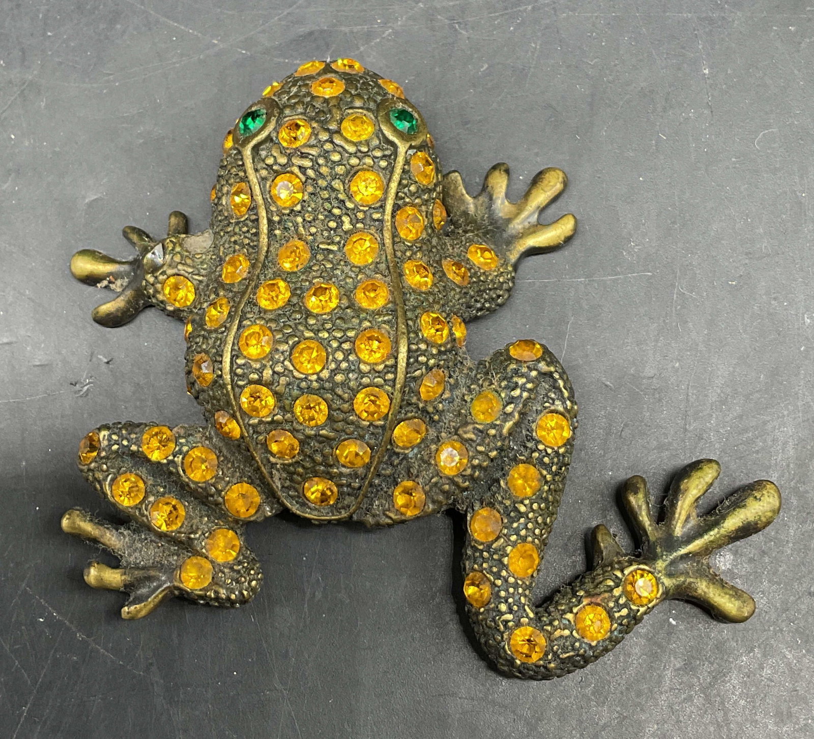 Vintage Gold Toned Rhinestone Frog Brooch: Vintage gold toned rhinestone frog brooch. Textured surface, frog figure. Accented with orange rhinestones and green rhinestone eyes. Measures approx 2.5 x 3 inches. Scratching, loss to rhinestones. J