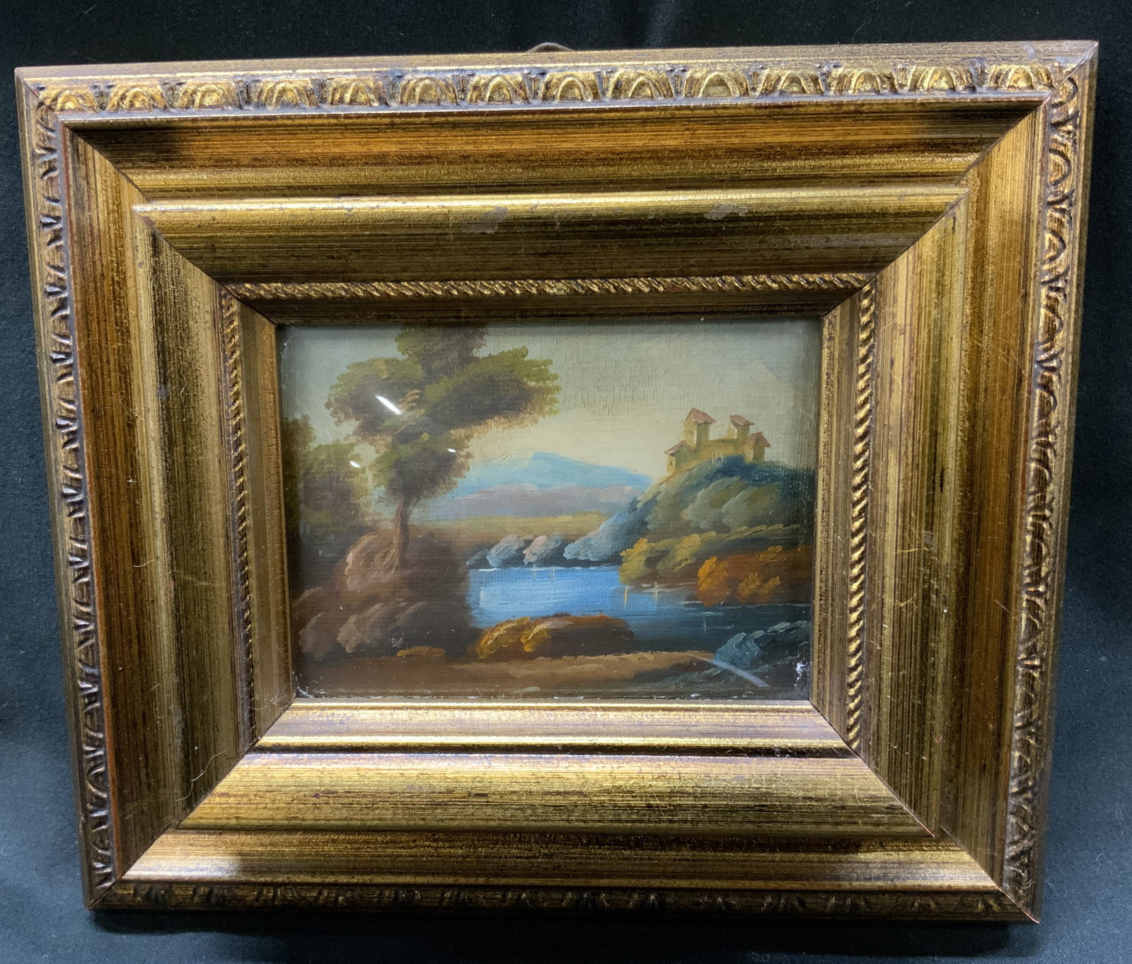 Sgnd Mini Pastoral Landscape Oil Painting Frmd: Signed mini still life oil painting on canvas. Signature reads illegibly. European countryside pastoral scene with house on top of hill, water, and trees. Frame, surface wear to frame, professionally 