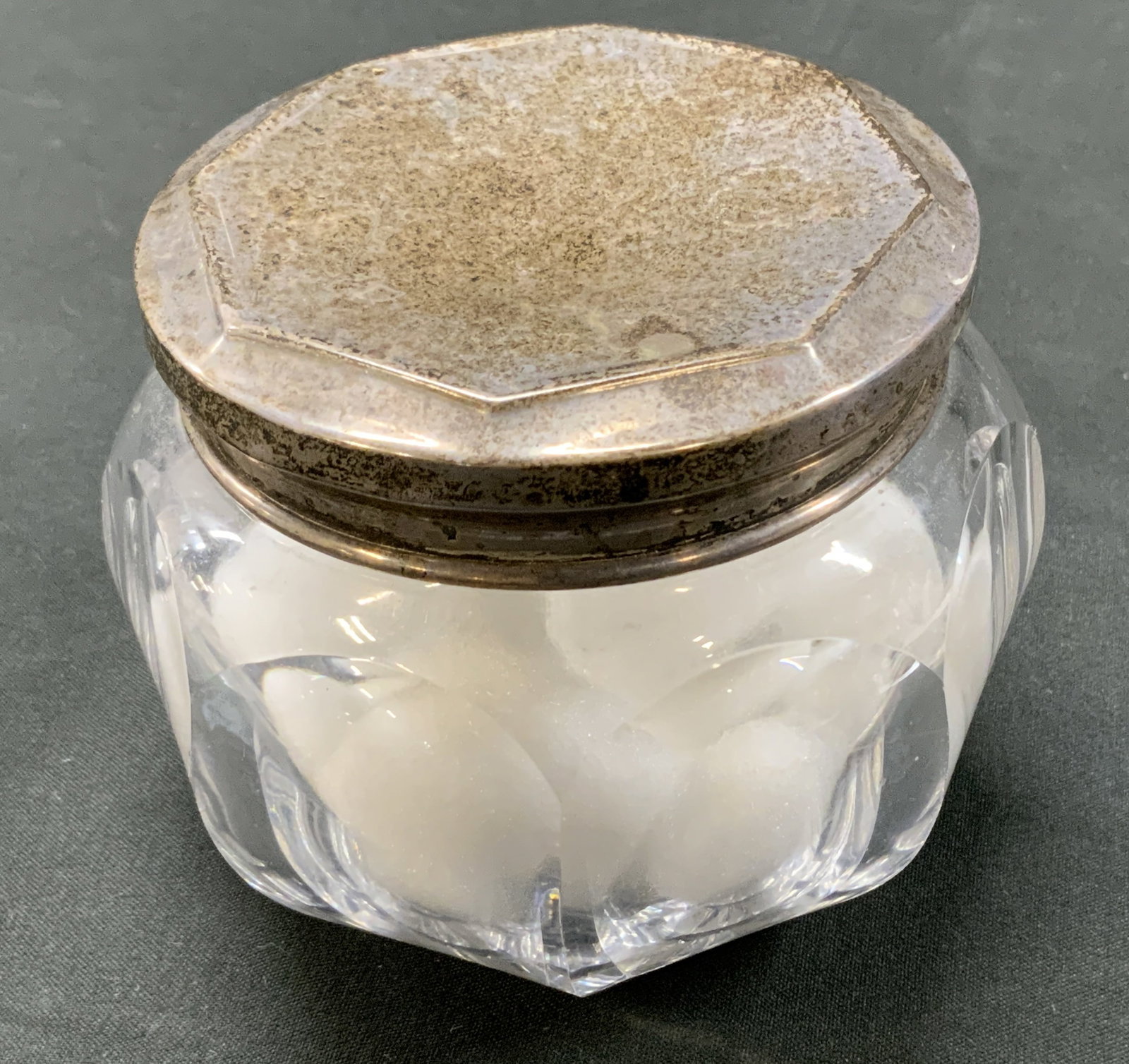 Antq Sterling Silver & Glass Vanity Jar: Antique cut glass vanity jar. Solid sterling silver lid designed with octagonal border. Thick walled glass base, cut with geometric facets. Condition consistent with age and exposure. Heavy patina on 