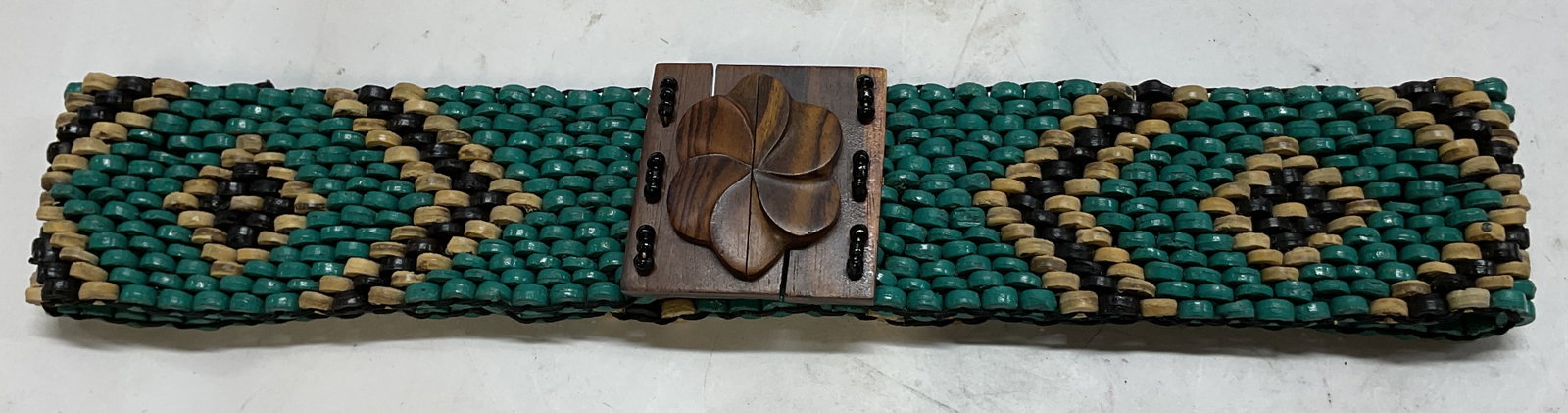 Hand Made Teal Beaded Stretch Belt: Hand made teal beaded stretch belt. Intricate geometric diamond pattern in teal, black, and tan. Carved wooden floral buckle. Measures approx 28 inches full length. Scratching. Belt, stretch belt, bea