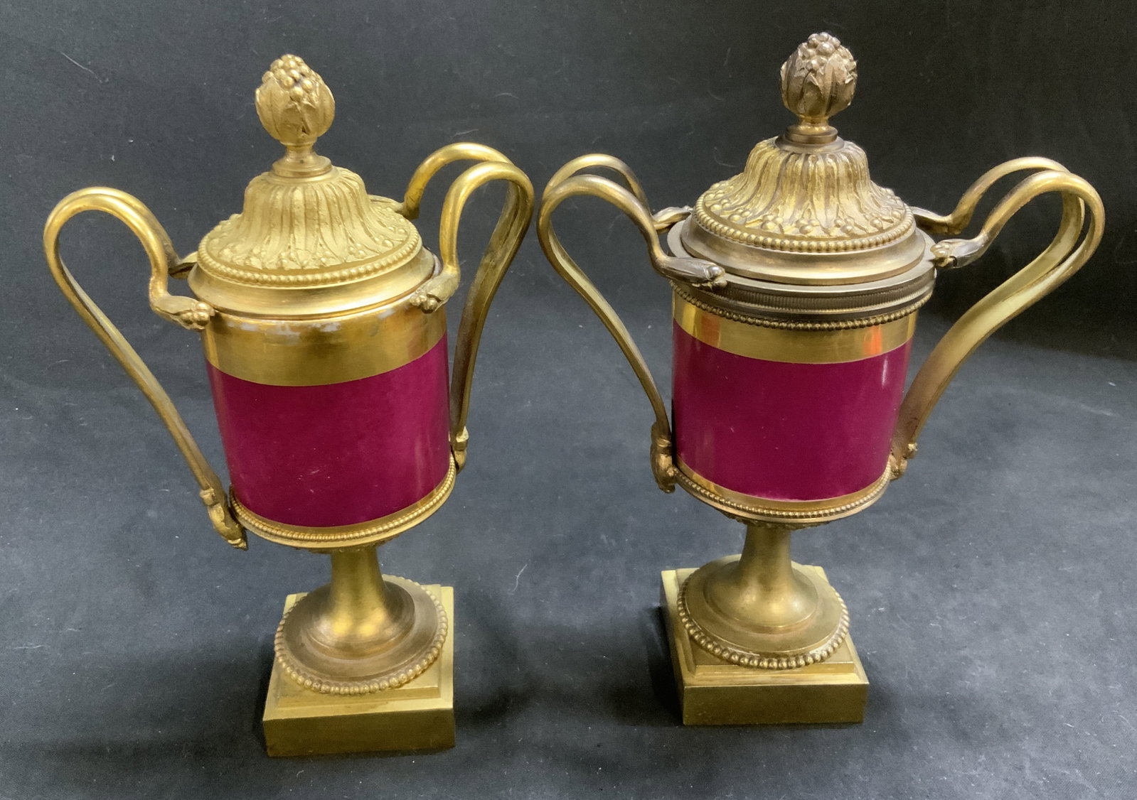 Pair Antq French Neoc-Sty Gilt Bronze Mantel Urns: Pair of Antique French Neoclassical-Style Mantel Urns. Burgundy enameled porcelain central body. Mounted inside highly detailed gilt bronze hardware. Some paint loss, chips, loose handles, missing har