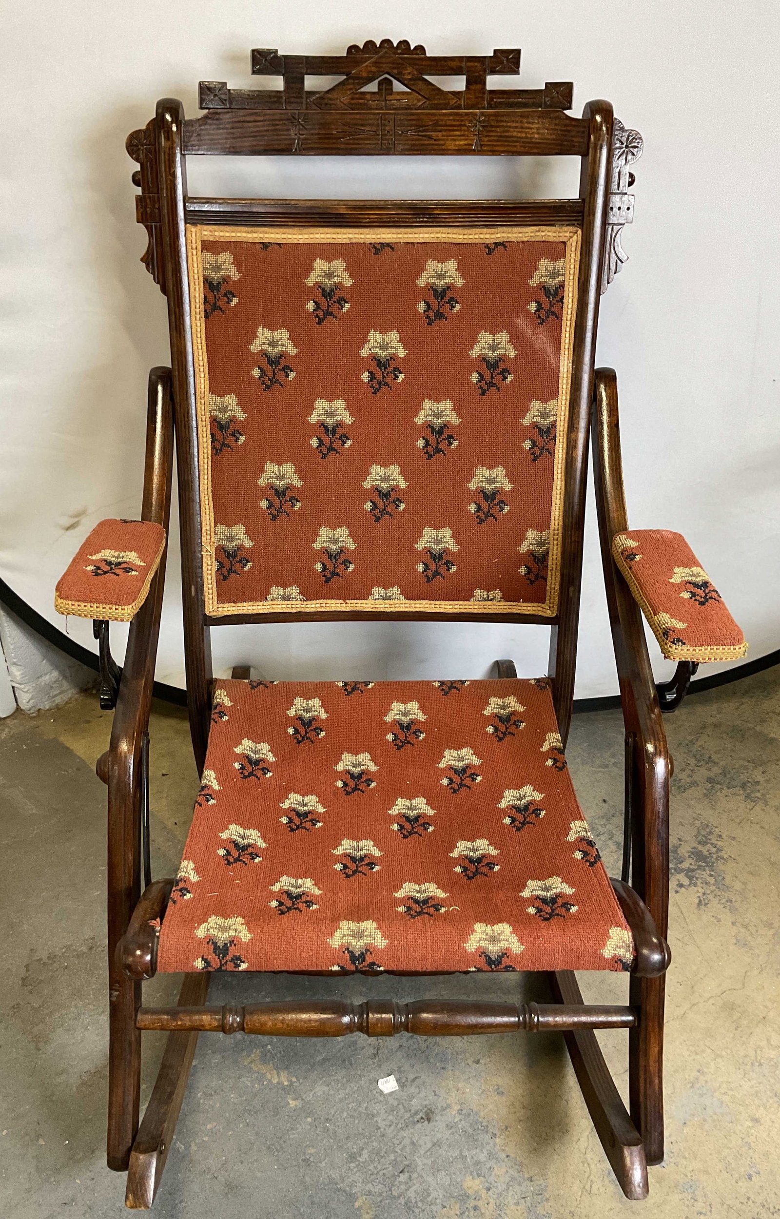 Antq Eastlake Style Wooden Folding Rocking Chair: Antique Eastlake style wooden folding rocking chair. Distinct geometric and stylized crest rail at the top. Accented with upholstered fabric. Orange background with repeating floral clusters. Lines