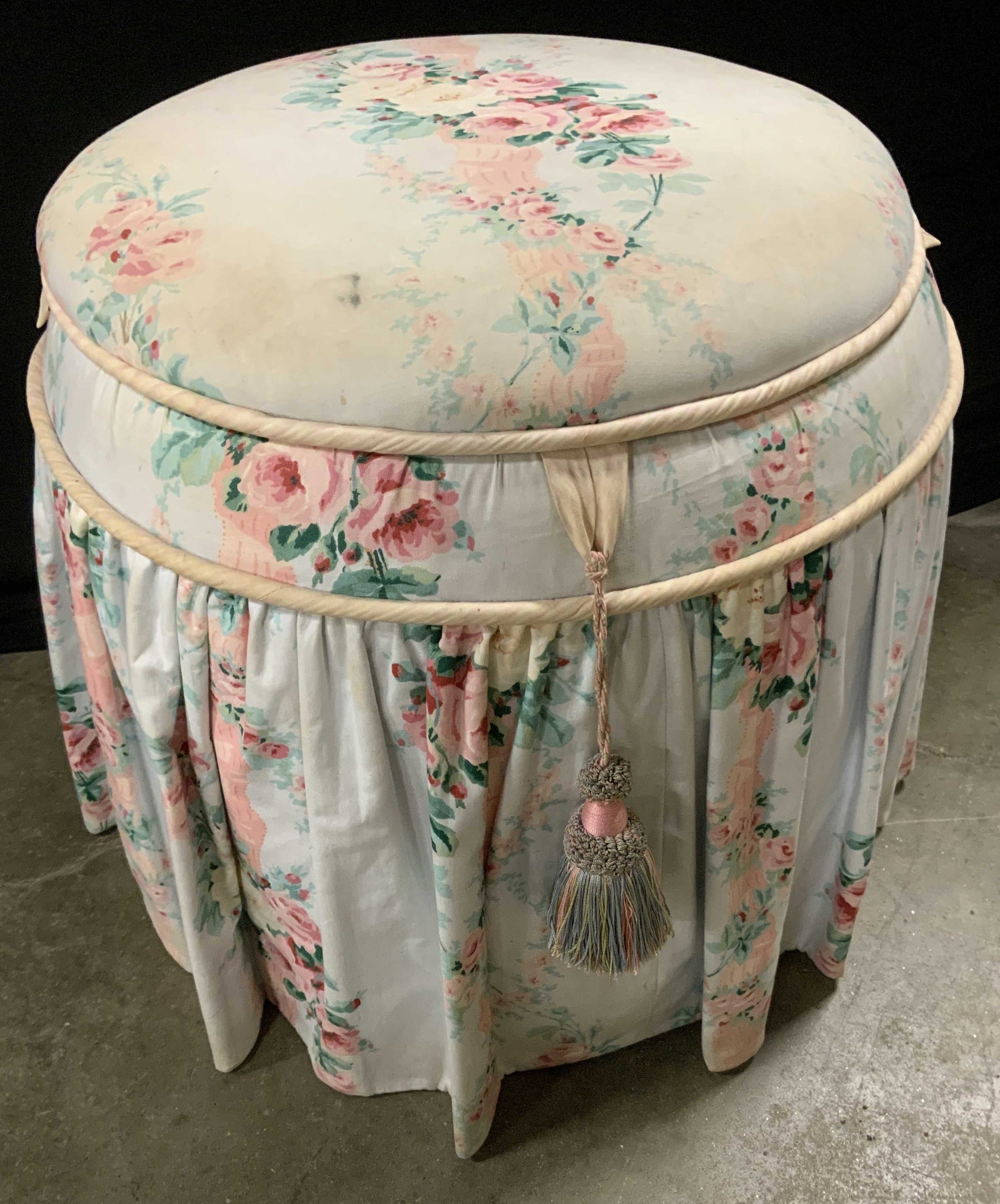 Chintz Upholstered Ottoman w Storage: Slip covered Chintz upholstered ottoman with storage, ruffle skirt, circular form, silk tassel and hinged lid fabric lined interior, fabric has wear and discoloration, measures app 18 inches, ht diame