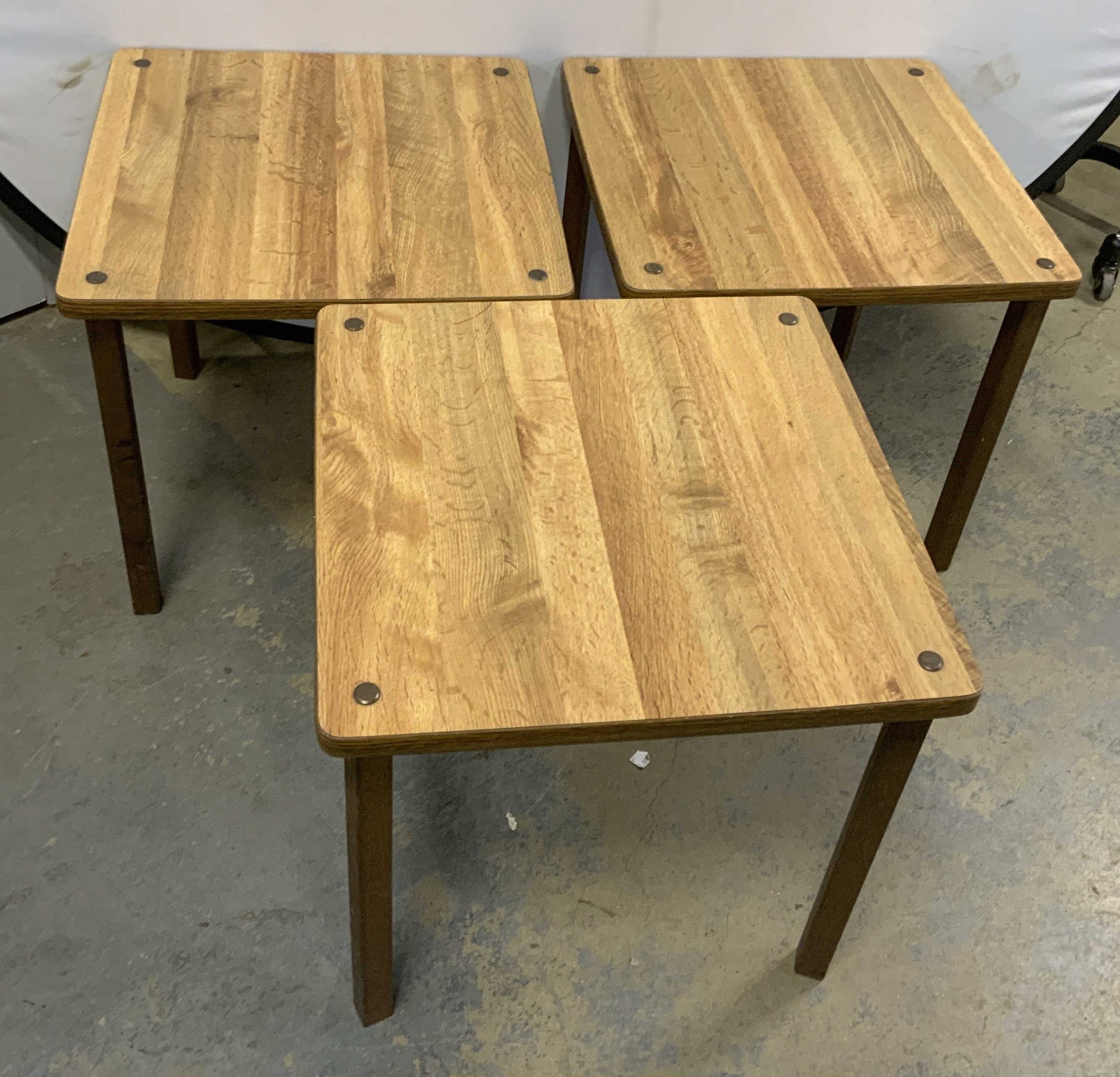 St3 Mid-Century Modern Wooden Table Set: Set of 3 Mid-Century Modern Wooden Tables. Butcher-Block Style Oak Veneer. Distinct grain patterns. Metal screw caps. Dark tapered legs. Condition consistent with age and exposure. Measures app 17in H