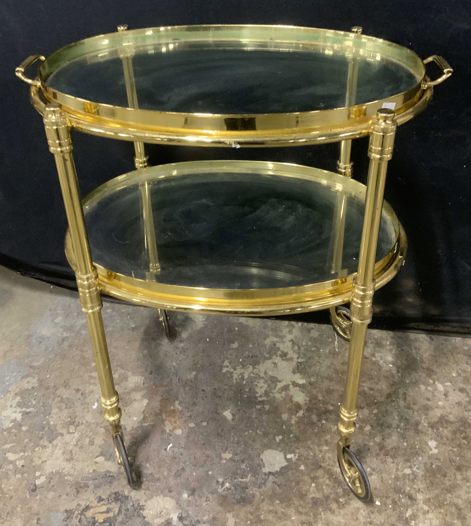 Vtg Hollywood Regency Dessert Trolley: Vintage Hollywood Regency Serving Trolley. Two-Tiered design. Oval glass with brass frame. Integrated push handle. Rolling caster wheels. Scratching and aging to metal present. Measures app 25in H x 1