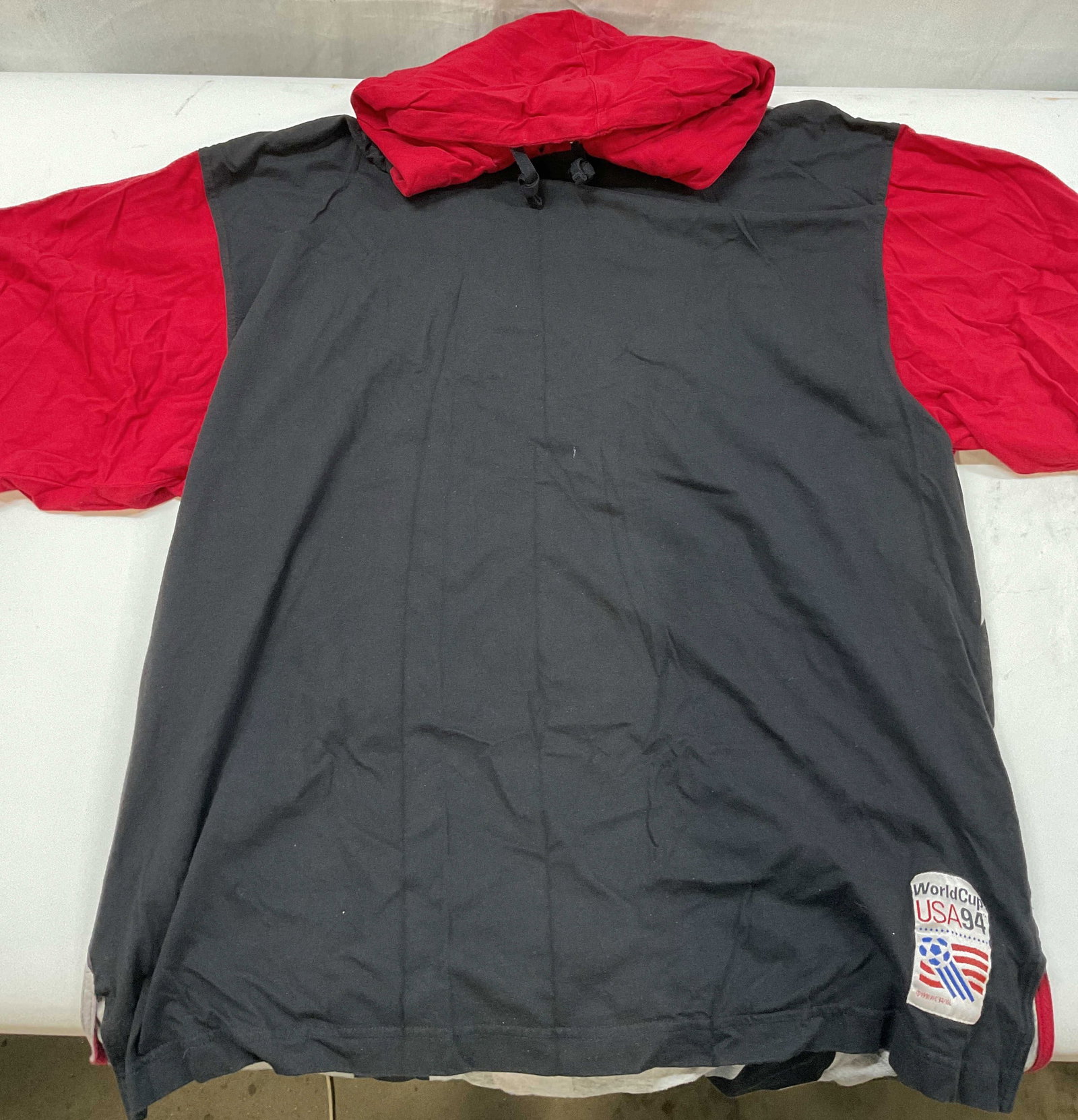 World Cup USA 1991 hooded t -shirt: World Cup USA 1991 hooded t -shirt. Shirt is a dark black body with bright red sleeve and red hood. The back is grey and black wavy vertical stripes. It features an official embroidered World Cup USA