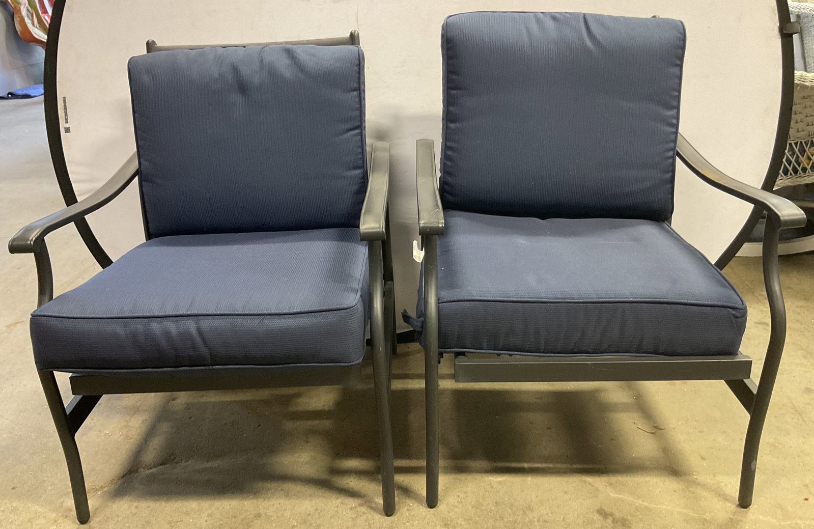 Pair Metal Cushion Outdoor Patio Armchairs: Pair of metal cushion outdoor patio armchairs. Black metal frame. Armrests curve downward. Curved and flared legs. Two thick navy blue cushions, seat and backrest. Textured ribbed pattern. Measures