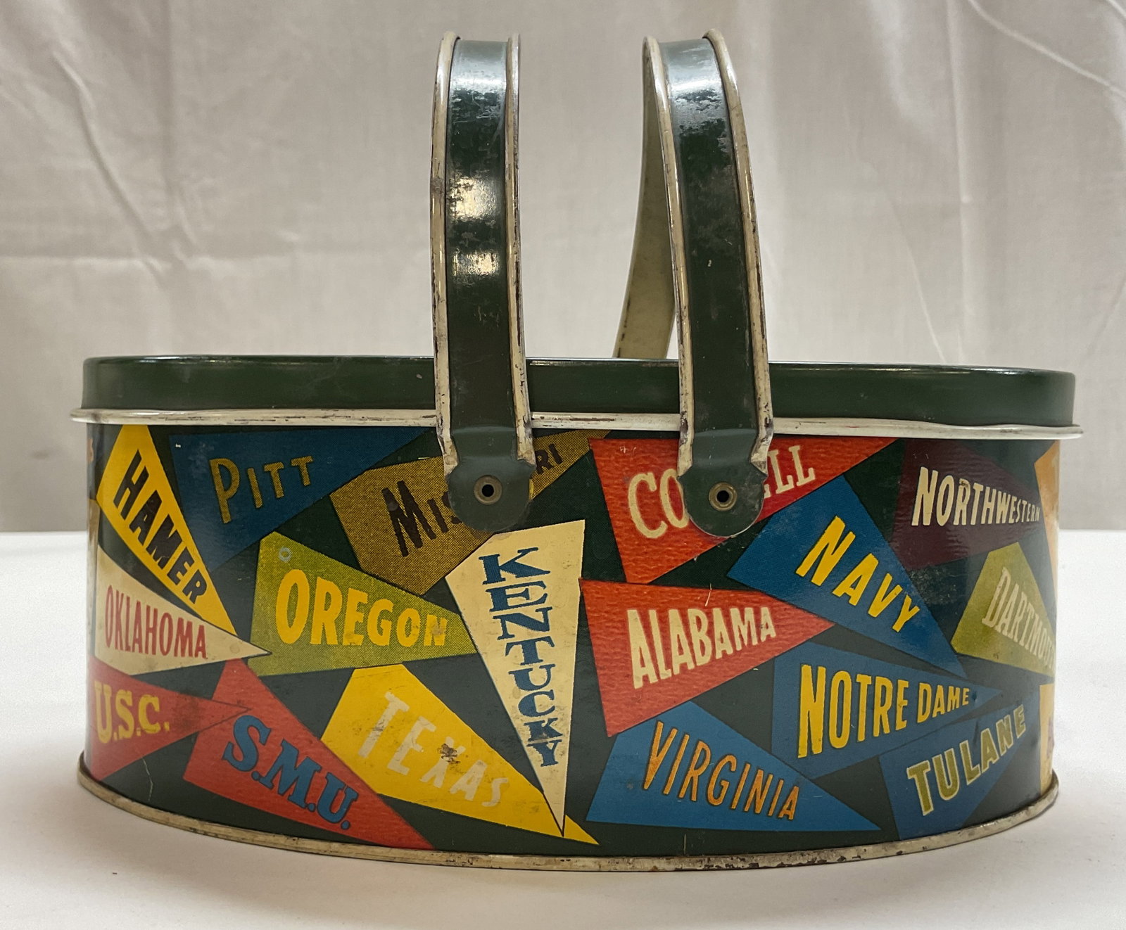 Vtg 1950s College Pennant Tin Litho Lunchbox: Vintage 1950s College Pennant tin litho lidded lunchbox. Oval shaped. Dark green lid and dual side swing handles. Features a colorful design of various university athletic banners. Some include Yale, 