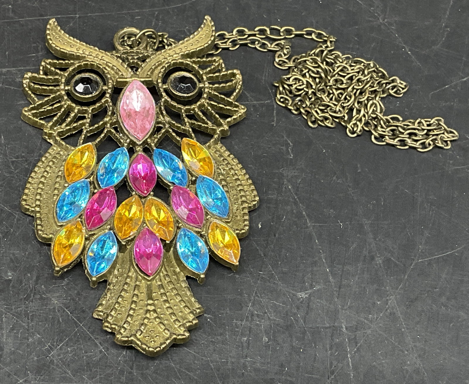 Vintage-Style Owl Pendant Necklace: Vintage-Style Brass-Toned Owl Pendant Necklace. Yellow, blue, and pink navette-cut rhinestone feather accents. Pink rhinestone beak. Black rhinestone eyes. Condition consistent with age and exposure.