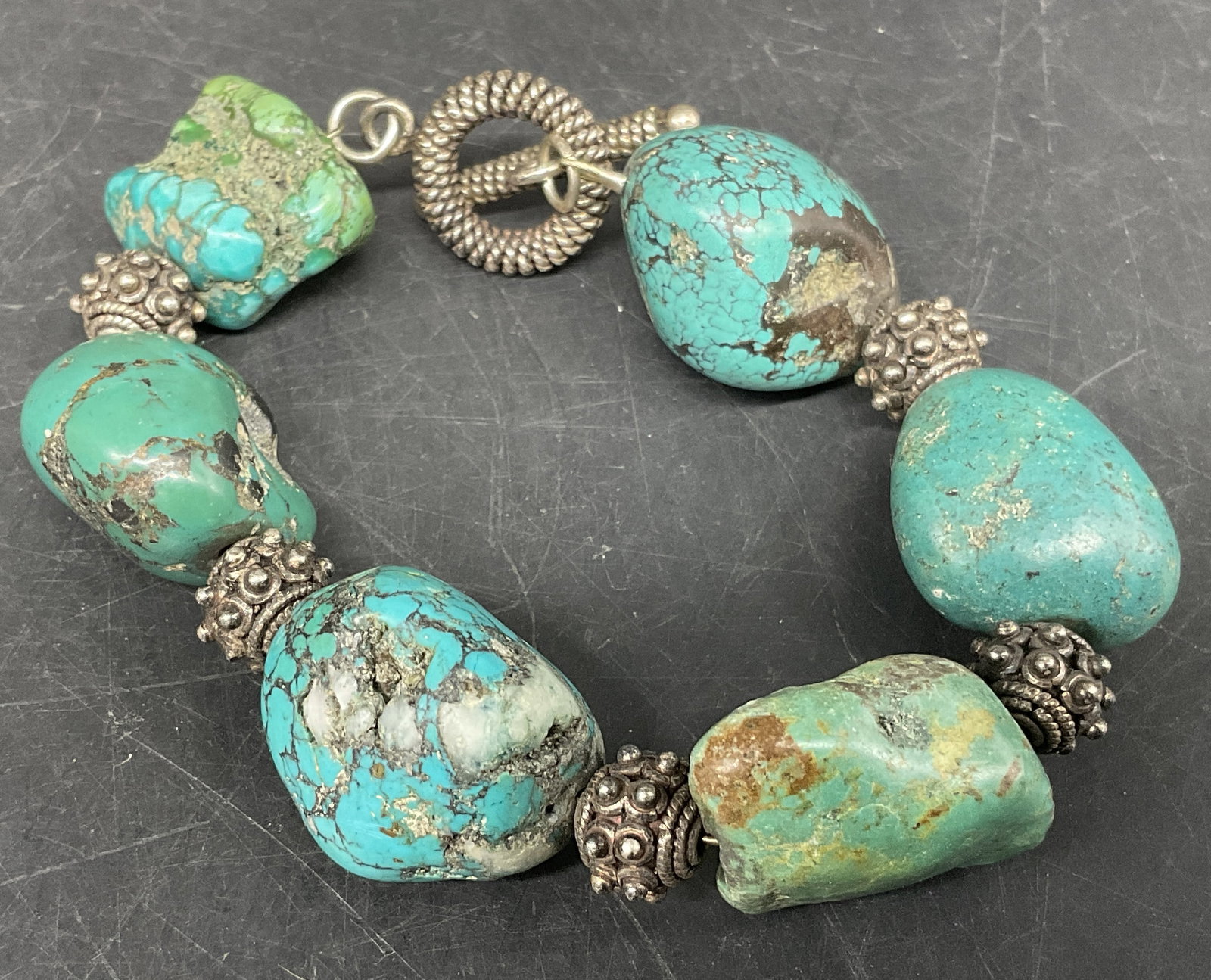 Turquoise-Toned Spacer Bead Toggle Bracelet: Turquoise-Toned Natural Stone Toggle Bracelet. Blue and green textured stones with silver-toned spacers. Condition consistent with age and exposure. Measures approx 7in L. turquoise-style, beaded, sil