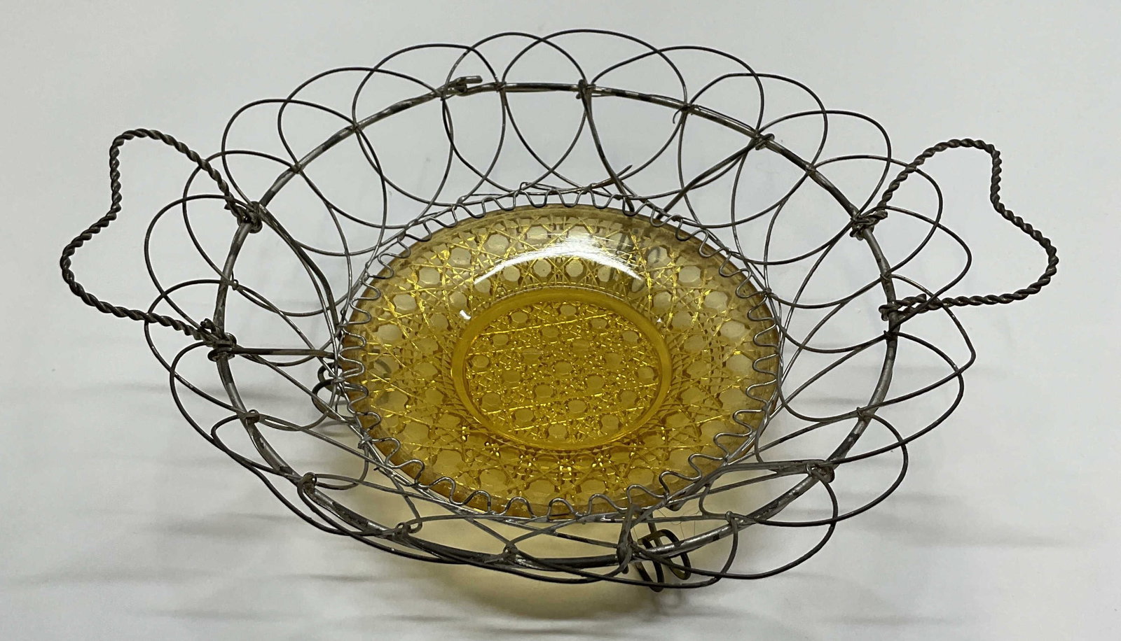 Antq Twisted Metal Wire & Glass Decorative Basket: Antique twisted metal wire and glass decorative basket. Footed on underside. Twisted design with handles on either side. Textured amber glass insert at the bottom. Measures ht approx 3 inches diam