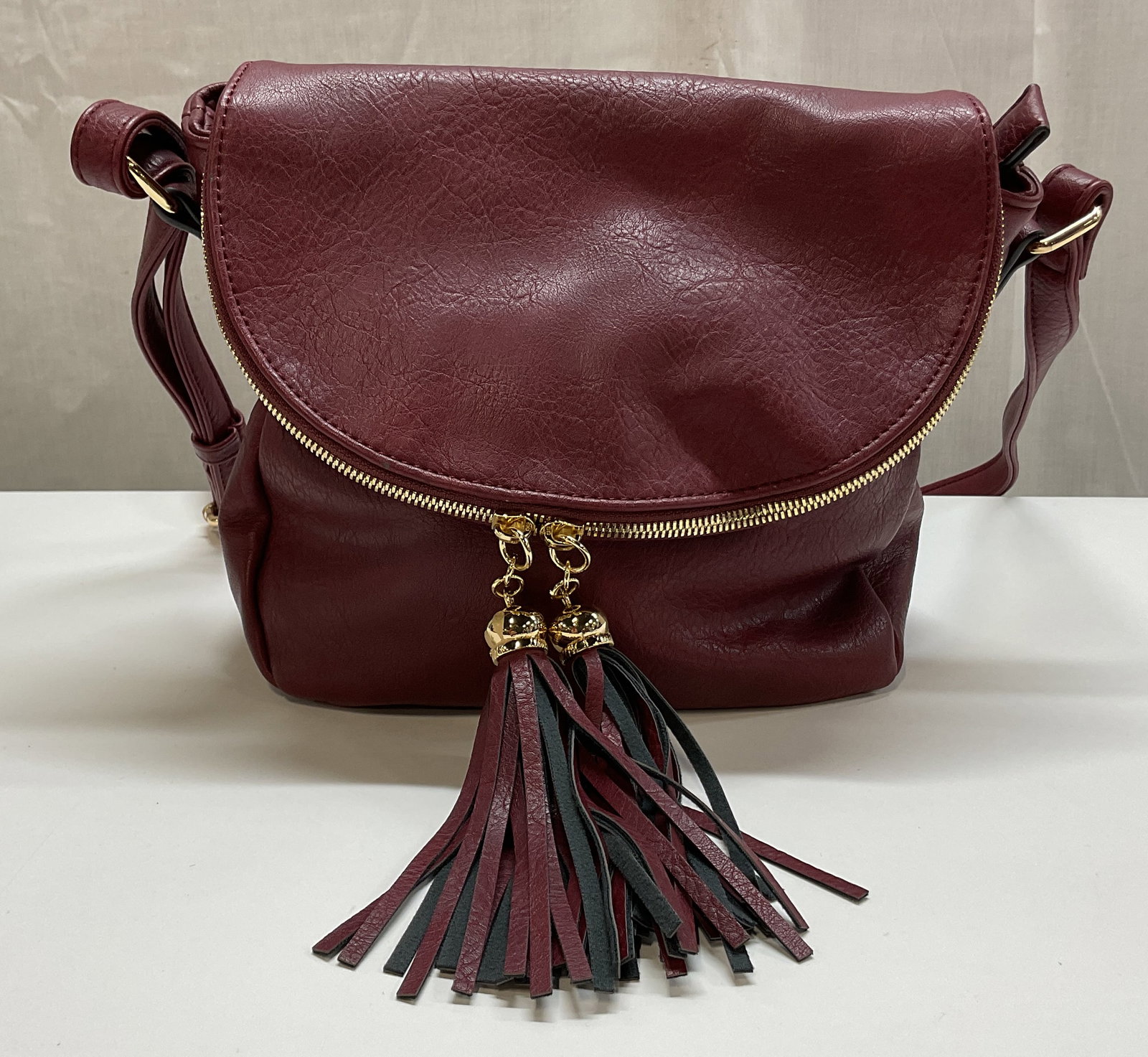 Vintage Fold Over Burgundy Crossbody Bag: Vintage fold over burgundy crossbody bag. Interior and exterior compartments with zippers. Attached strap with buckle design. Fold over flap with magnetic button closure. Burgundy and black tassel