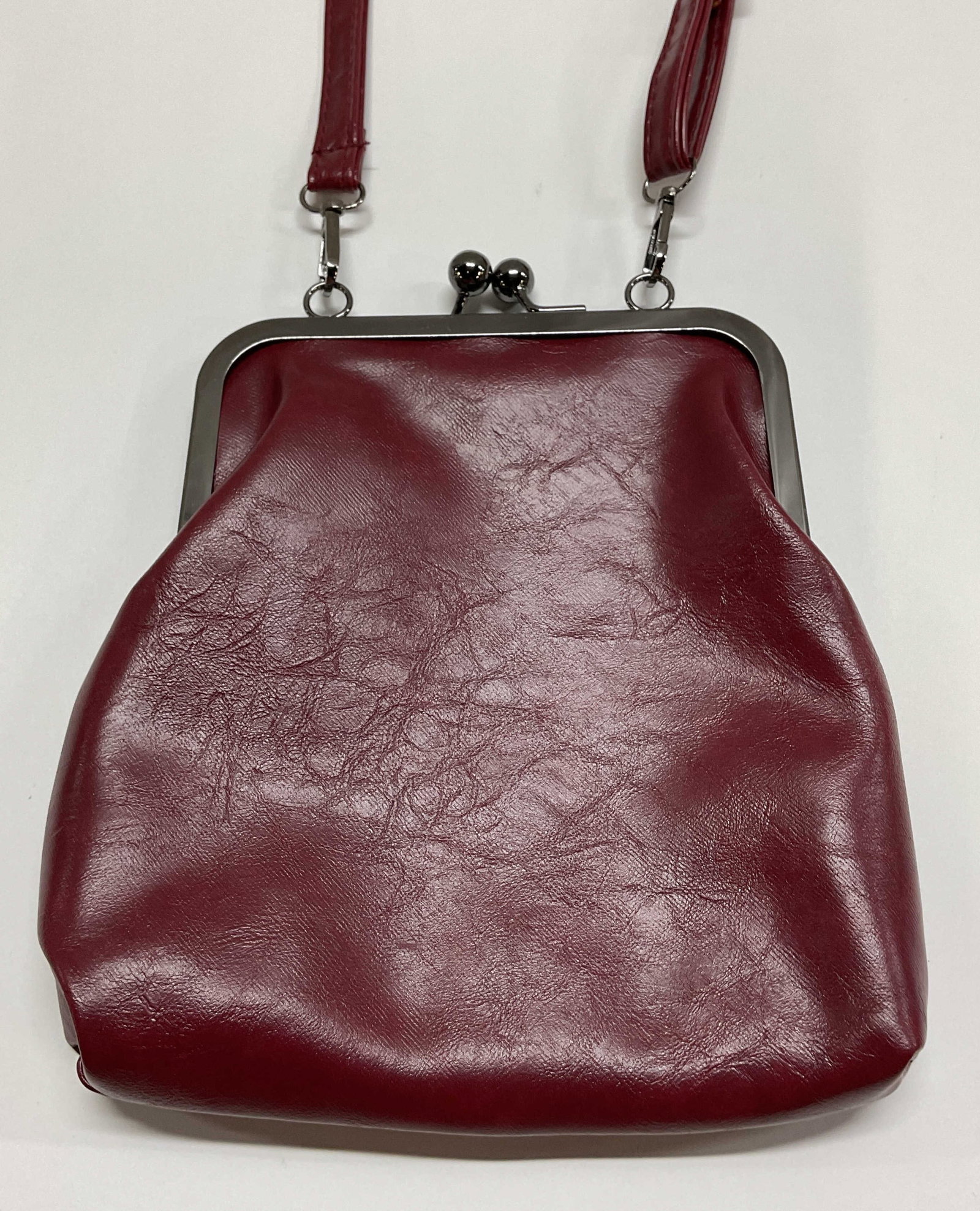 Vintage Burgundy Crossbody Bag: Vintage burgundy crossbody bag. Attached strap with buckle design. Unique clasp closure and interior compartments. Comes with additional handle strap. Measures approx 8 x 9.5 inches. Surface wearing