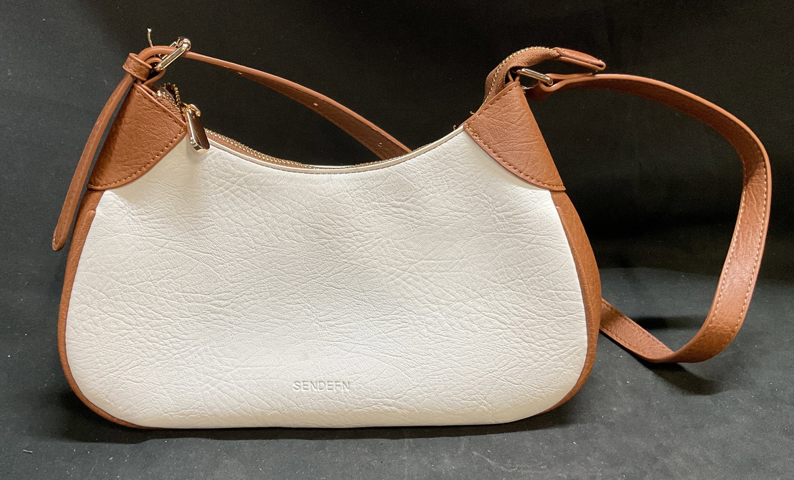 Sendefn White & Brown Shoulder Purse: Sendefn white and brown shoulder purse. Crescent shape. Attached strap with buckle design. Top zipper and interior compartments. Main white body with brown trim. Measures approx 6 x 11 inches.