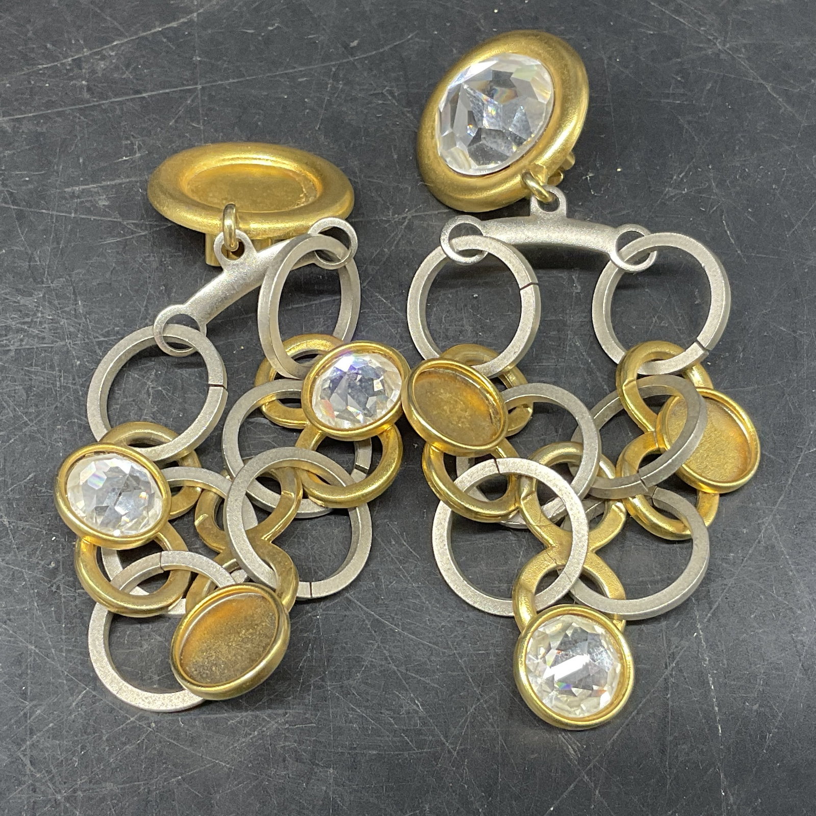 VTG 80s Dannah Chandelier Dangle Earrings: Vintage Circa 1980s Dannah Clip-On Earrings. Silver-Toned and gold-toned multi-ring chandelier dangle design. Clear rhinestones. Missing Stones. Measures approx 3.5in L. vintage, clip-on earrings,
