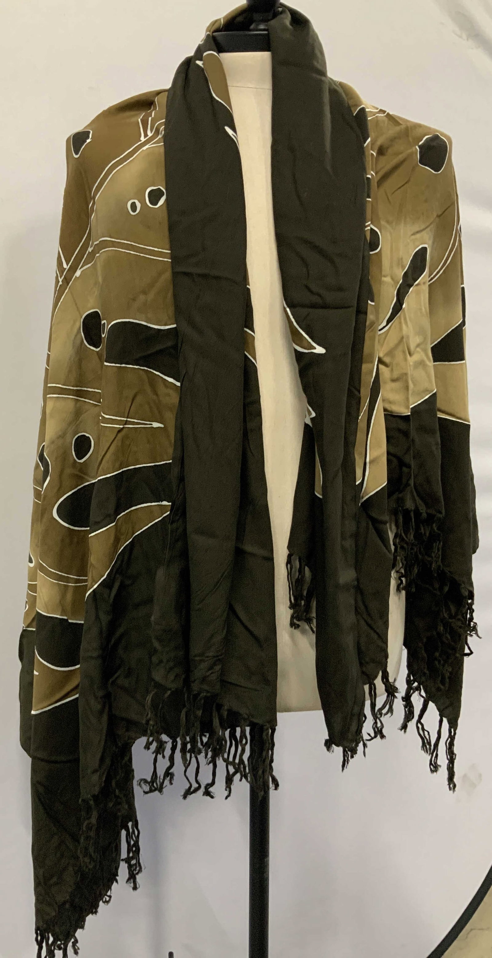 Tropical leaf fringe fashion wrap: Tropical leaf fringe fashion wrap. Features a large scale golden monstera deliciosa leaf. Earth toned color scheme leaves on dark brown background. The fabric has a relaxed flowing drape with an open 