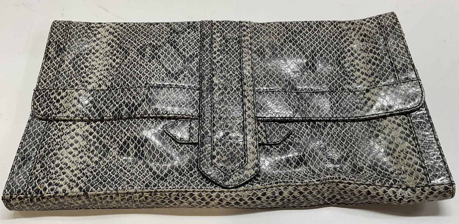 Auslini Snakeskin Style Large Clutch: Auslini snakeskin style large clutch. Magnetic closure. Interior compartments. Black and white snakeskin style pattern. Fold over flap design. Measures approx 8.5 x 15 inches. Surface wear consistent 