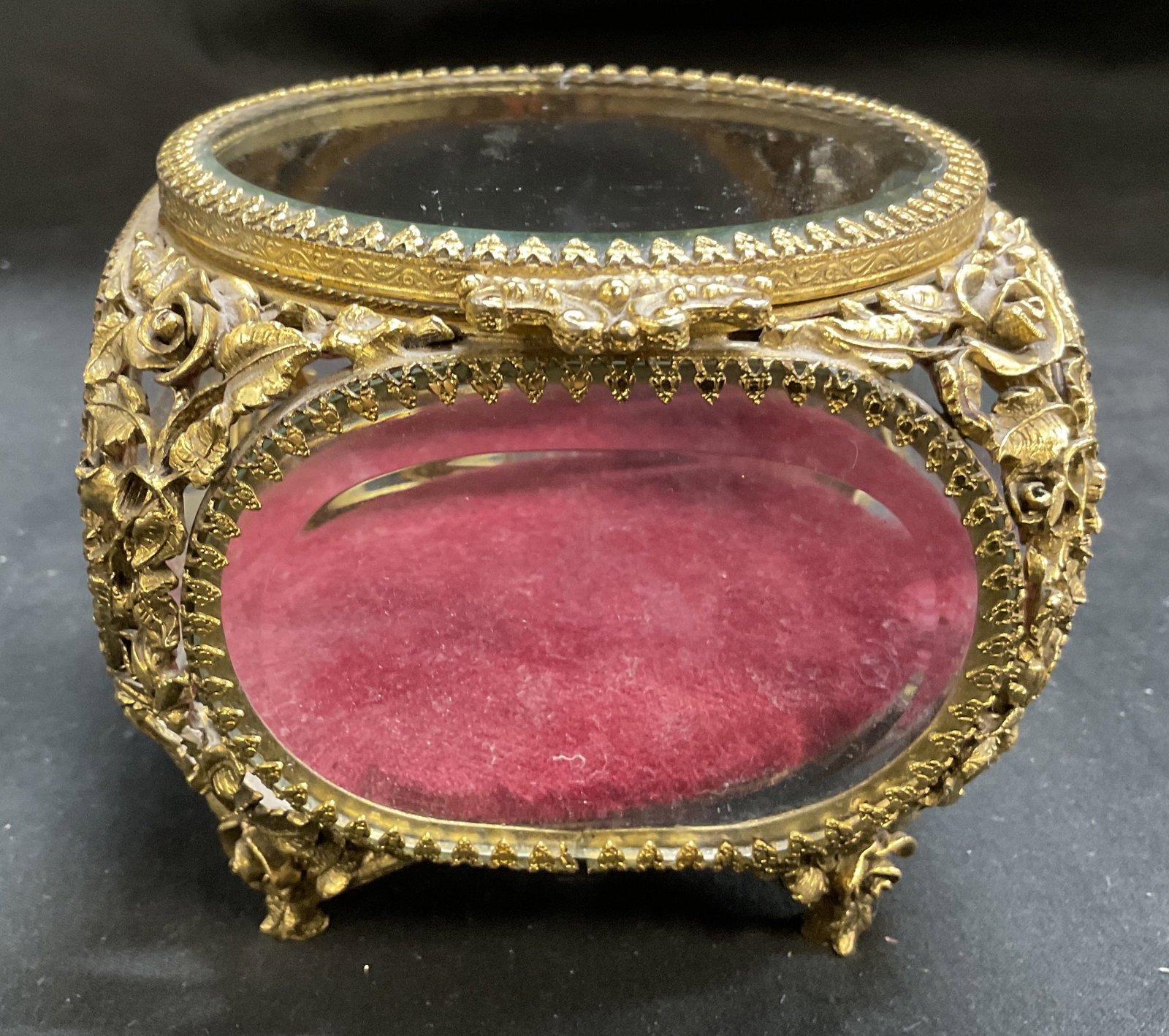 Hollywood Regency Bevel-Glass Jewelry Casket: Vintage Hollywood Regency Bevel-Glass Jewelry Casket. Gilt filigree frame with scrolling and roses relief work. Four glass viewing panels. Red velvet cushion interior. Condition consistent with age an