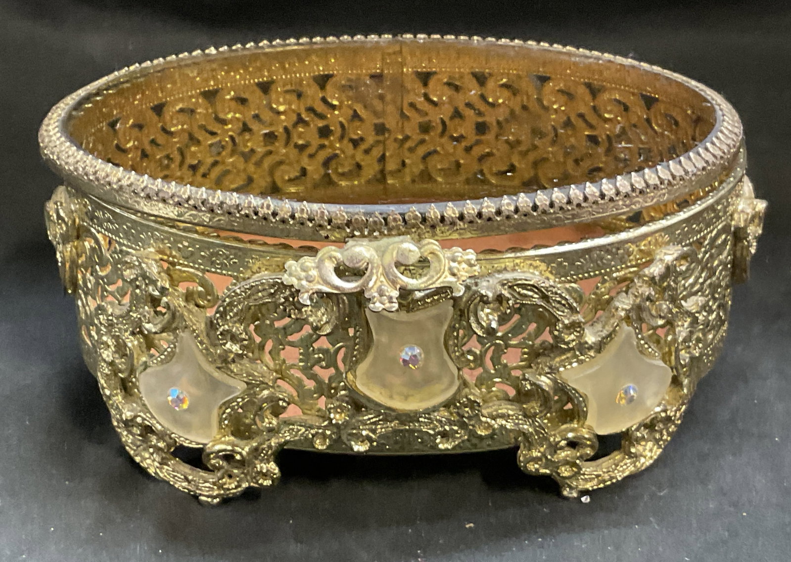 Hollywood Regency Gilt Filigree Jewelry Casket: Hollywood Regency Gilt Filigree Jewelry Casket. Intricate scrollwork. Oval glass top. White glass accents with rhinestones. Condition consistent with age and exposure. Measures approx 6in Diam. Hollyw