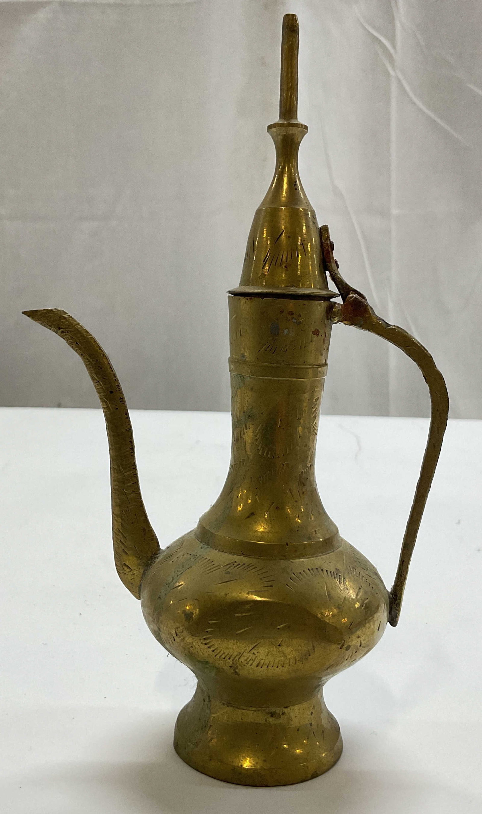 Vintage Indian Etched Brass Ewer: Vintage Indian etched brass Ewer. Round pedestal base. Long curved spout and handle. Hinged lid with decorative finial. Etched pattern. Measures ht approx 8 inches diam approx 2 inches. Scratching and