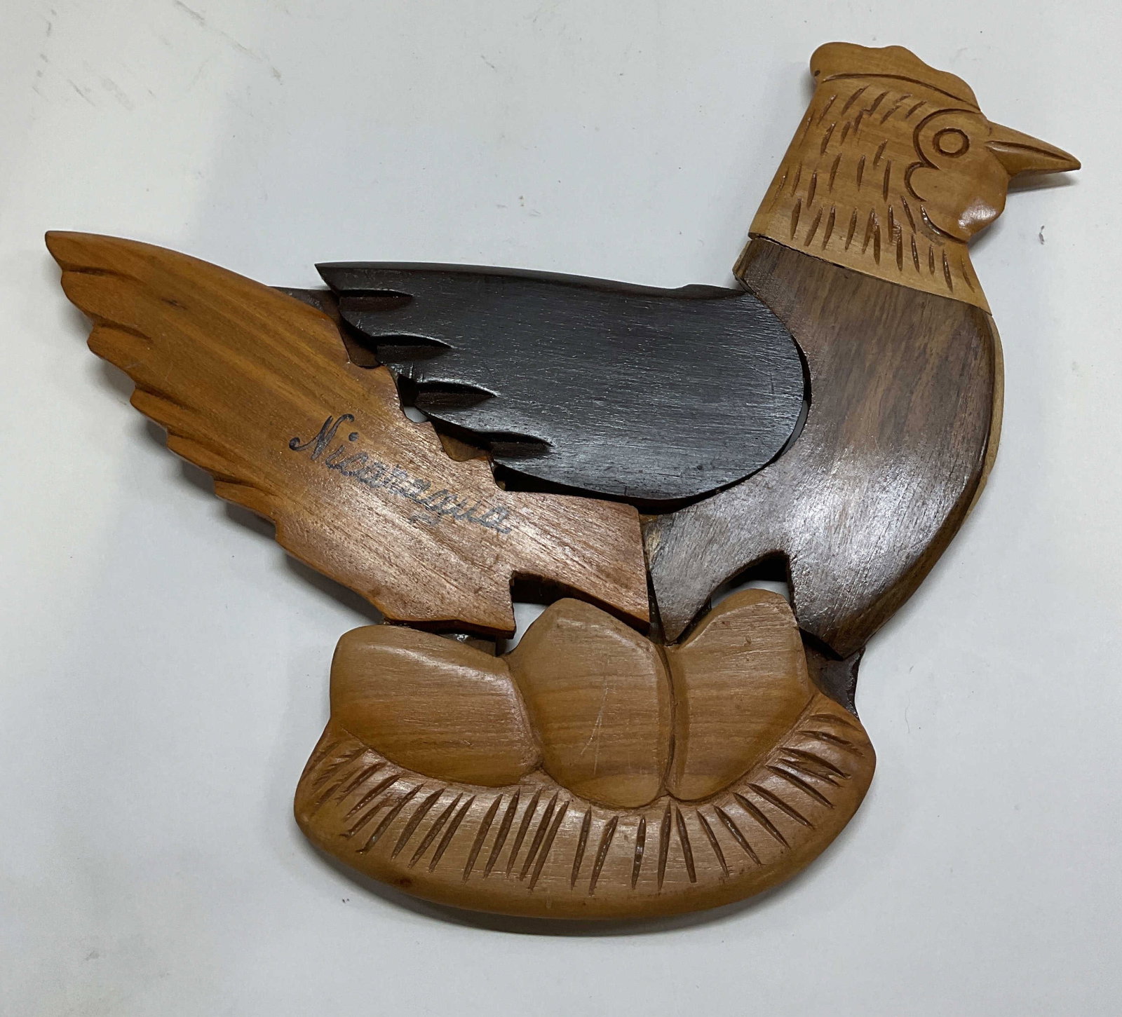 Hand Crafted Wooden Intarsia Puzzle Chicken Decor: Hand crafted wooden intarsia puzzle chicken decor. Inscribed Nicaragua on surface. Chicken figure laying on a nest of eggs. Hand carved details and features. Contrasting tones. Different pieces fit to