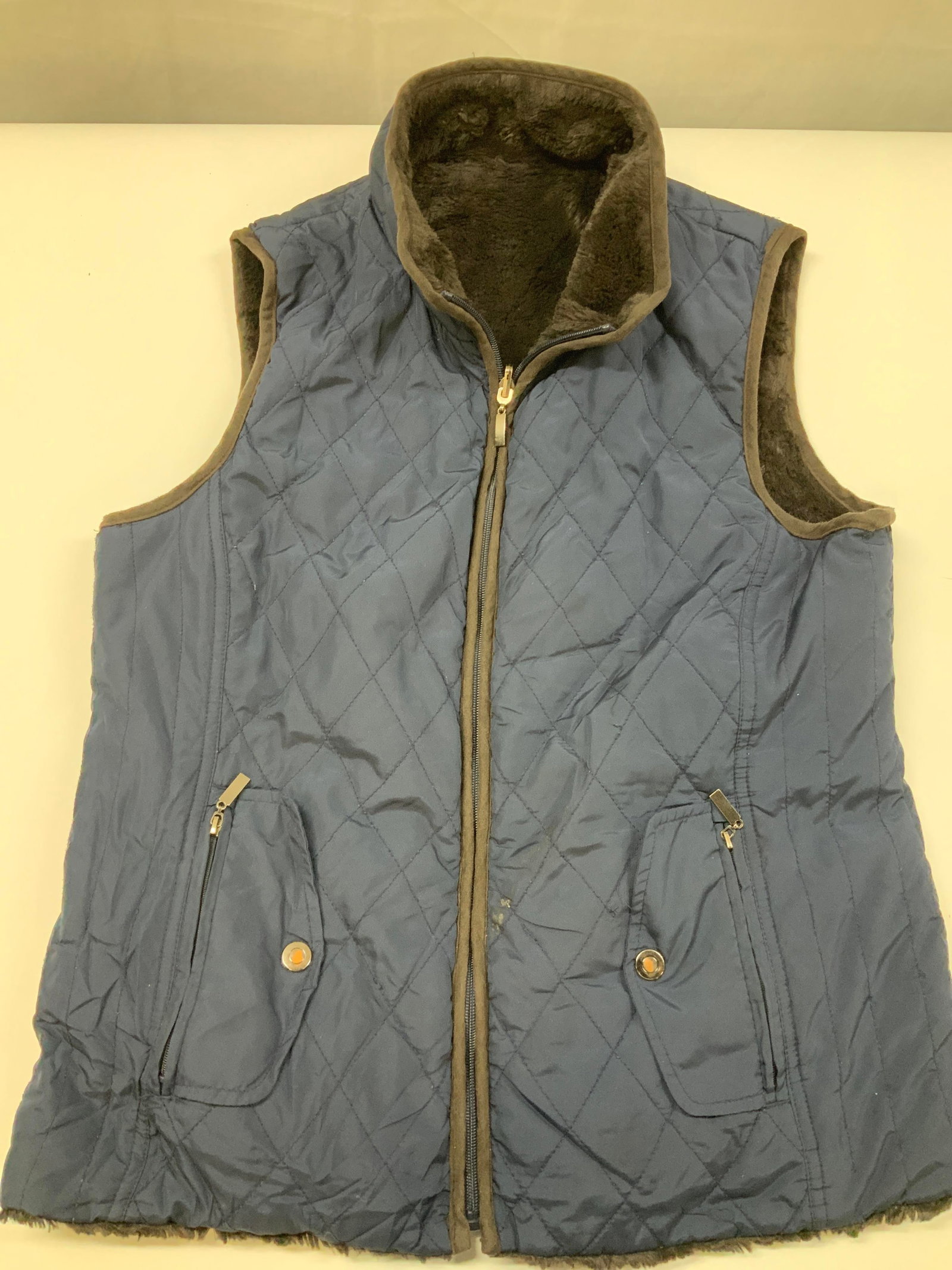 Navy blue diamond quilted outerwear vest: Navy blue diamond quilted outerwear vest. Features a traditional diamond quilt stitch pattern that adds pattern while also providing insulation. Lined entirely with a soft dark brown faux fur