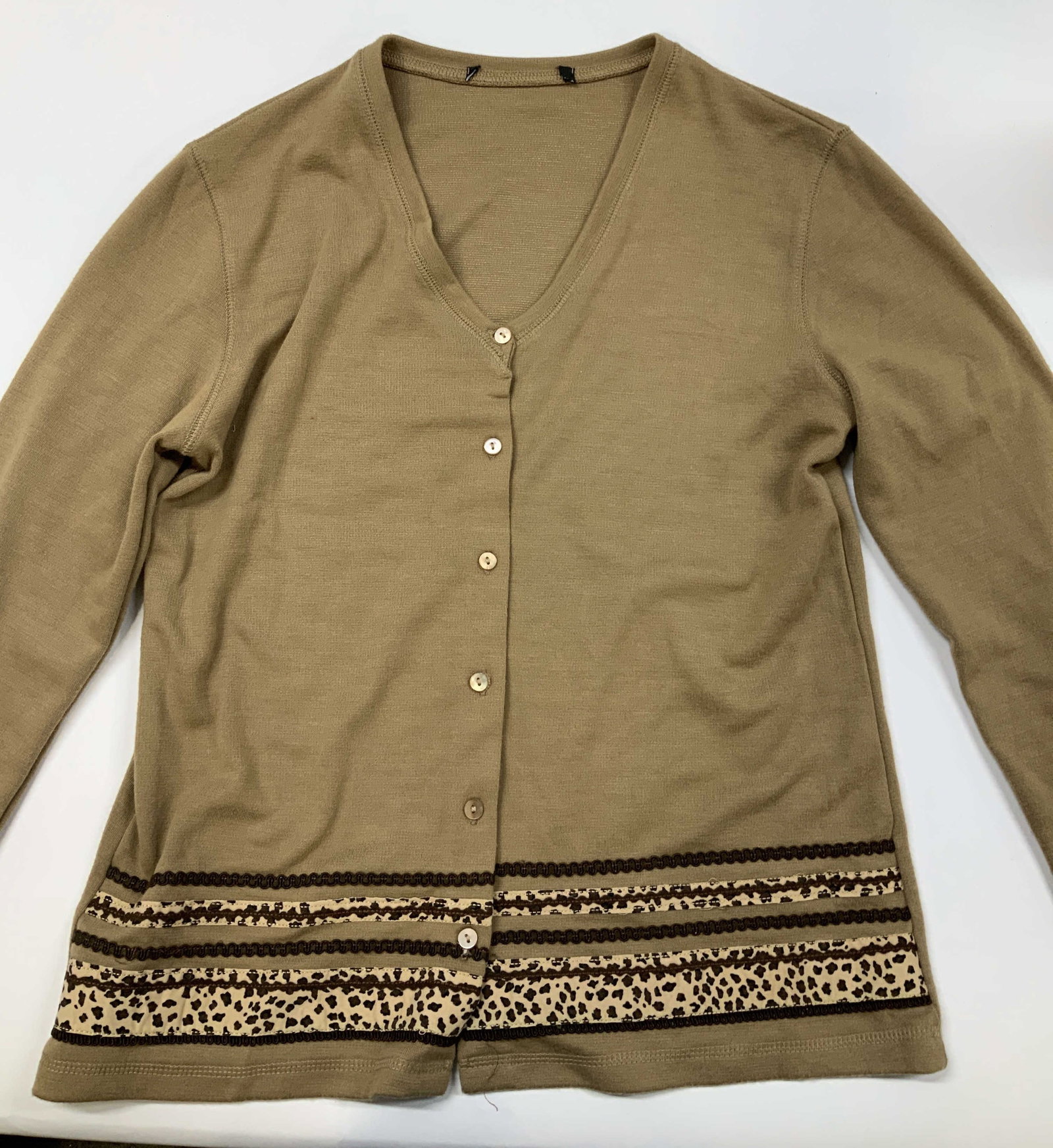 Tan v neck cardigan with leopard print detail: Tan v neck cardigan with leopard print detail. Features a deep v neckline, Classic button down front with color matched buttons and long sleeves. The standout feature is the multilayered border detail