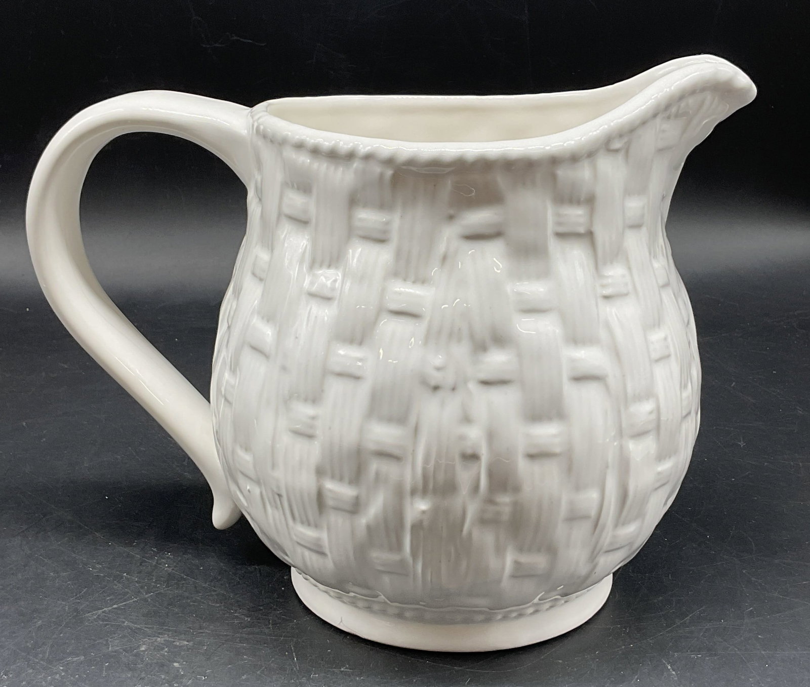 Neuwirth White Glazed Ceramic Pitcher Portugal: Neuwirth white glazed ceramic pitcher. Marked on underside, reads Made In Portugal For Neuwirth. Curved handle and spout. Basketweave pattern. Beaded pattern rim. Textured surface. Glossy finish. Meas