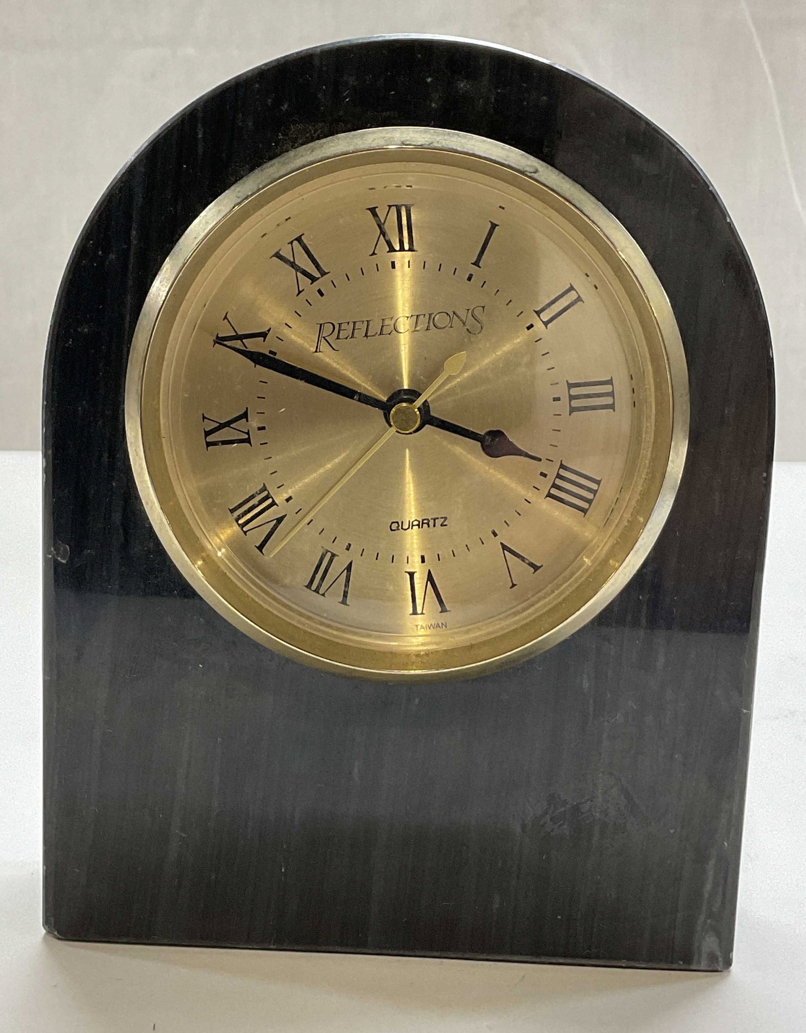 Reflections Black Marble Arch Desk Clock: Reflections black marble arch desk clock. Arched design. Gilt rim clock face with Roman numerals. Some weight. Measures approx 1.5 x 5 x 6.5 inches. Not tested for function, sold as is. Scratching.