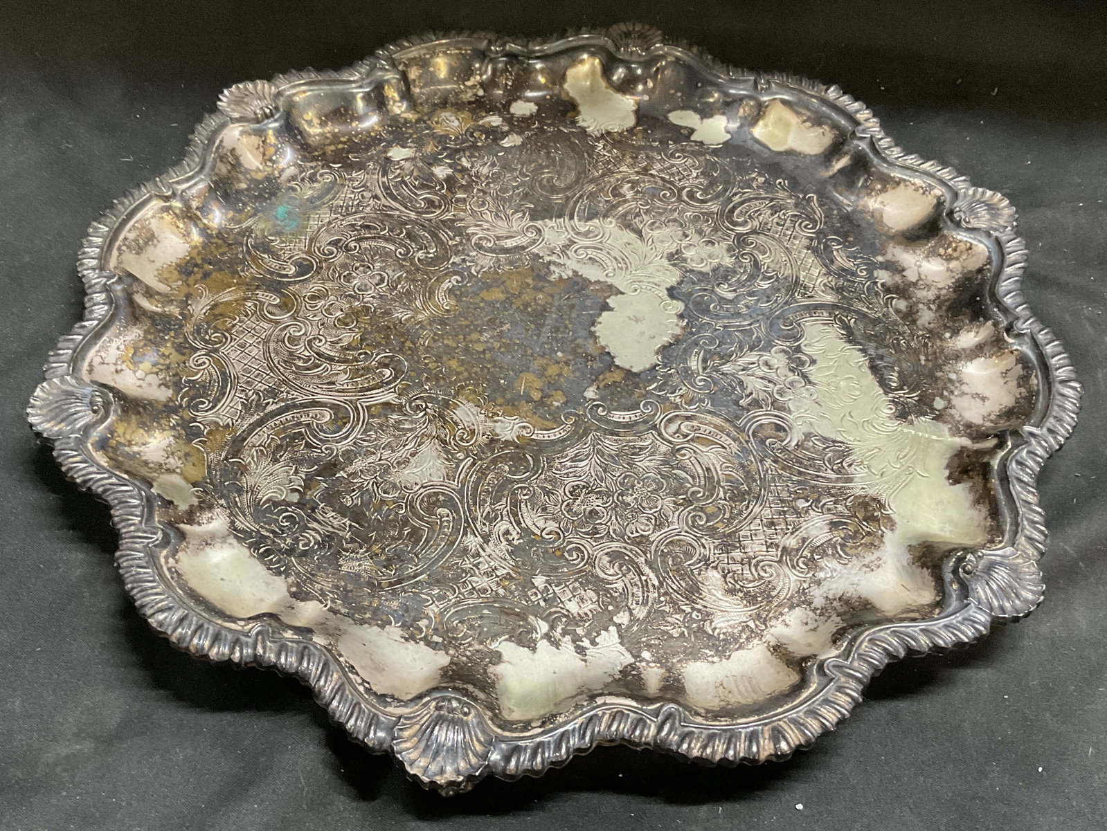 ANTIQUE Silver-Plated Round Butler Tray: Antique, Possibly Vintage Silver-Plated Round Butler Tray. Embossed scroll and floral patterns. Scalloped rim. Shell accents. Tarnishing, plating loss, and oxidization present. Measures approx 11.5in 