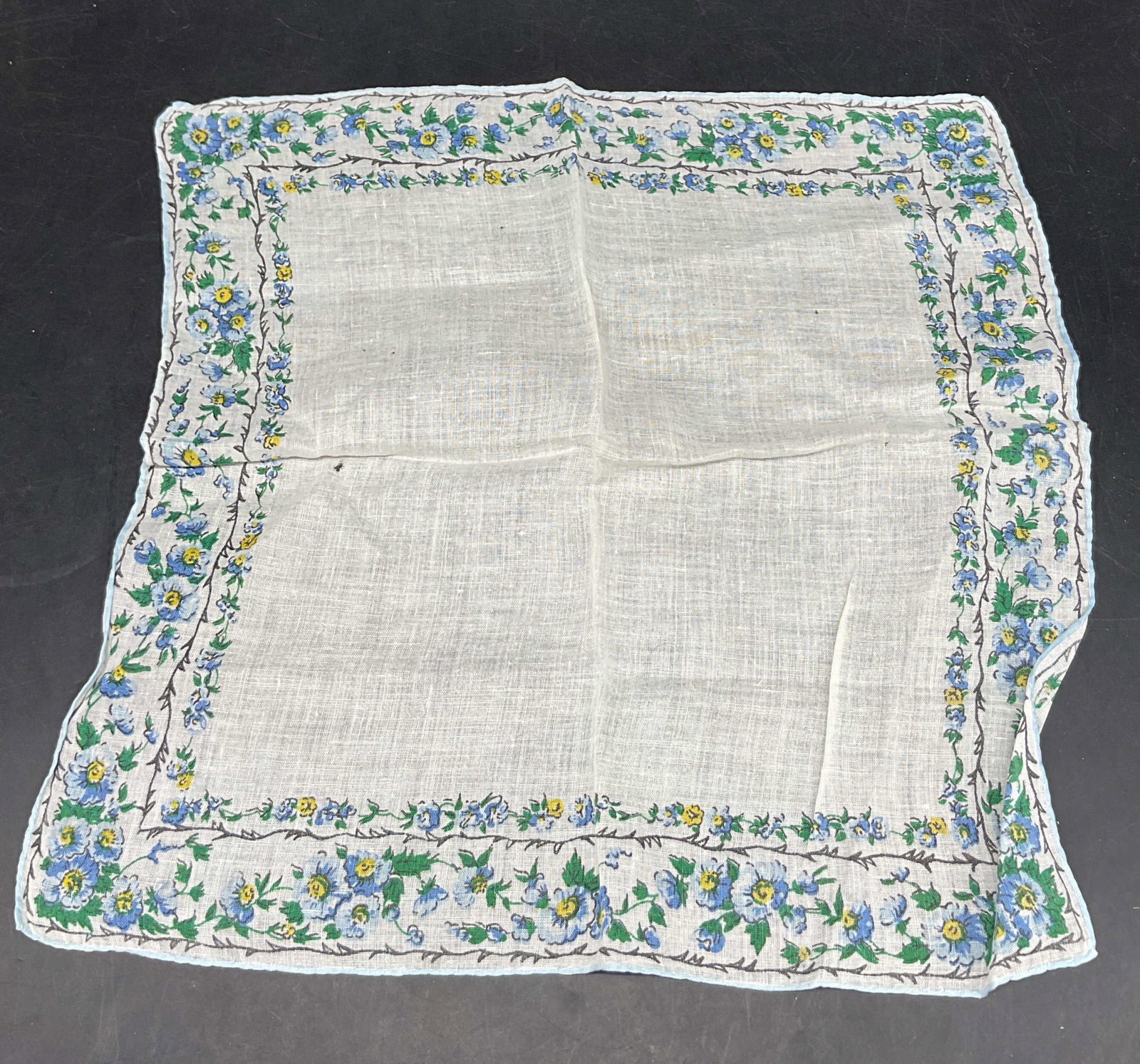Vintage White Floral Linen Napkin: Vintage white floral linen napkin. Floral motif border in blue, green, yellow. Black leaf motif border. Measures approx 12 x 12.5 inches. Small holes in fabric. Napkin, linens, tableware, home decor, 